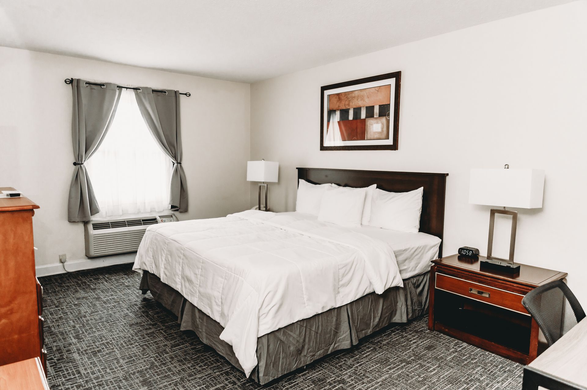 Hotel bedroom with a bed, nightstands, a chest of drawers, and a window with gray curtains.