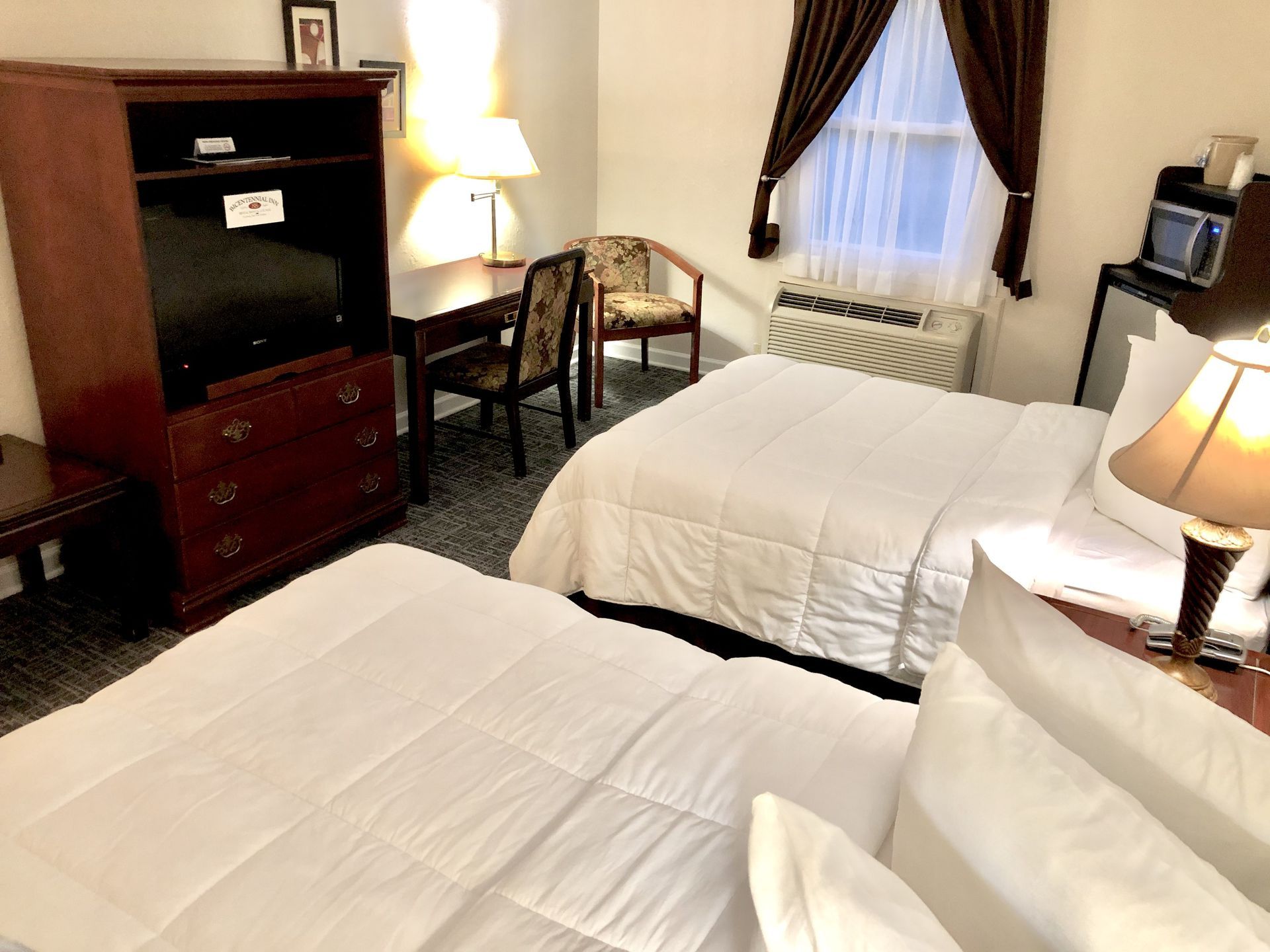 Hotel room with two beds, a desk, and a wardrobe with a TV.