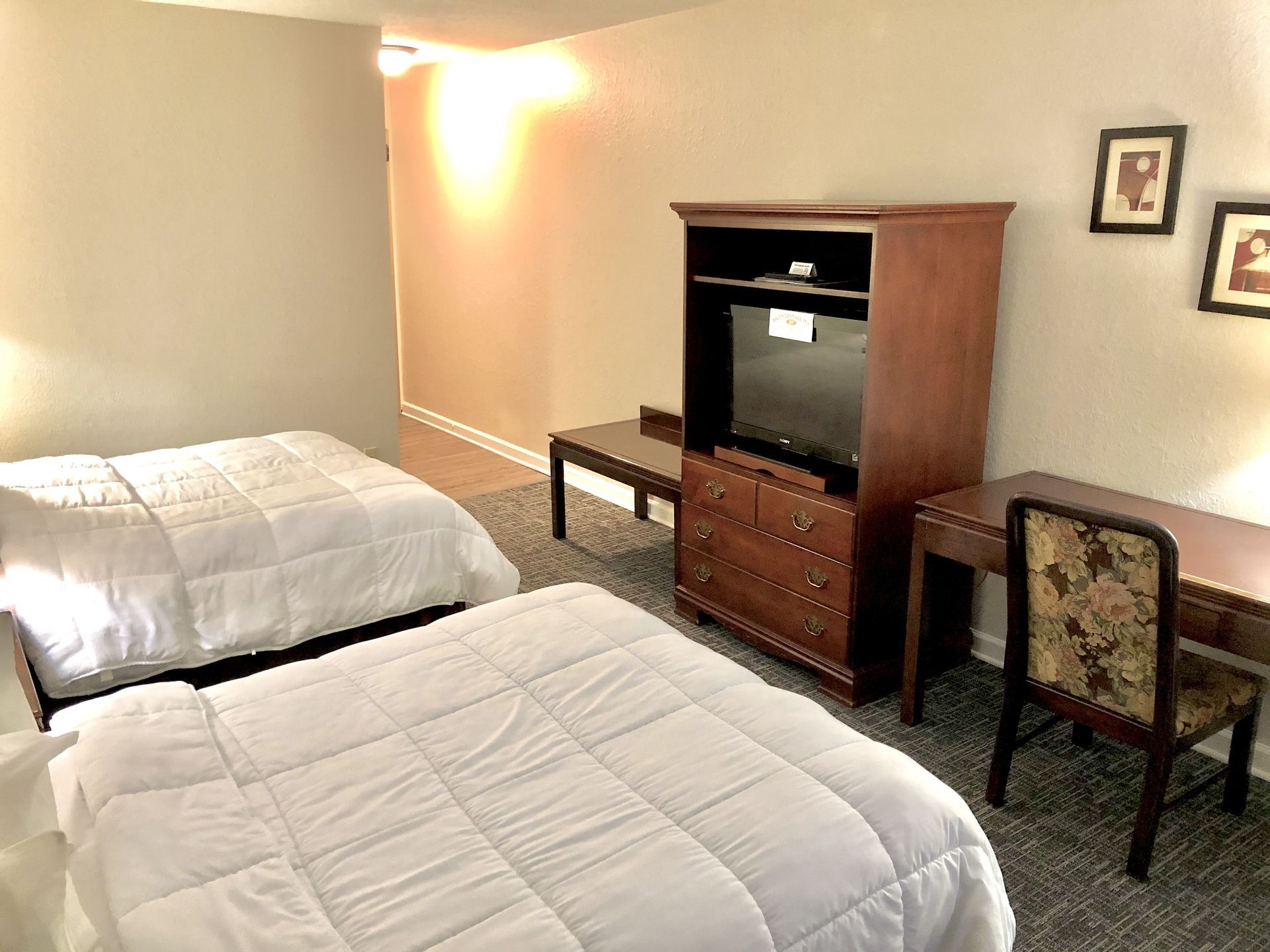 Two twin beds, TV cabinet, desk in a hotel room. Beige walls, brown furniture, carpet.