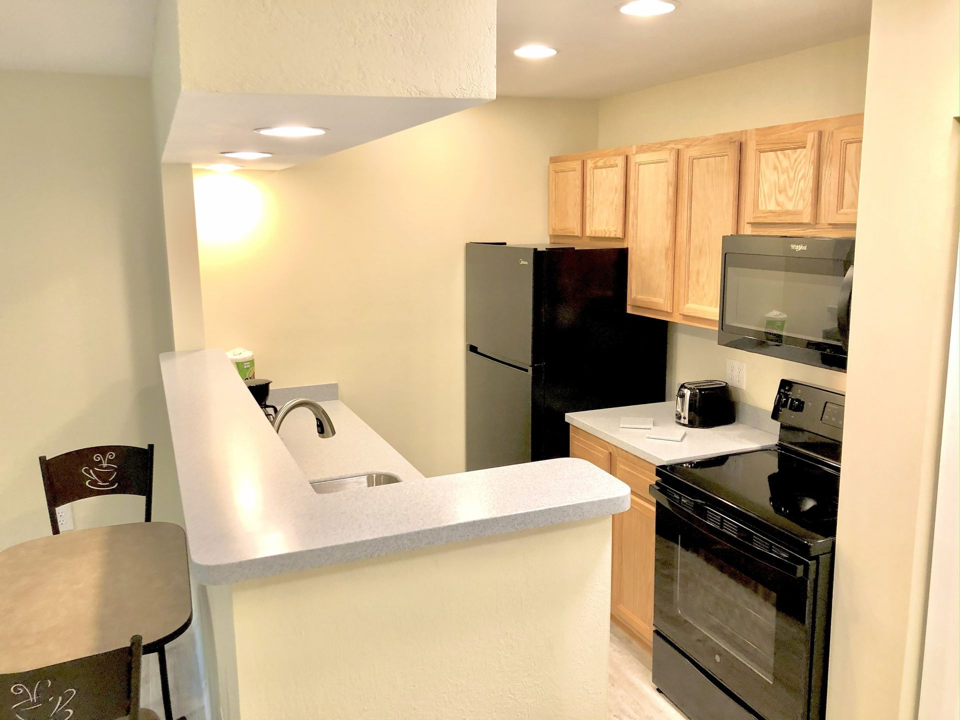 Small kitchen with light wood cabinets, black appliances, and a breakfast bar.
