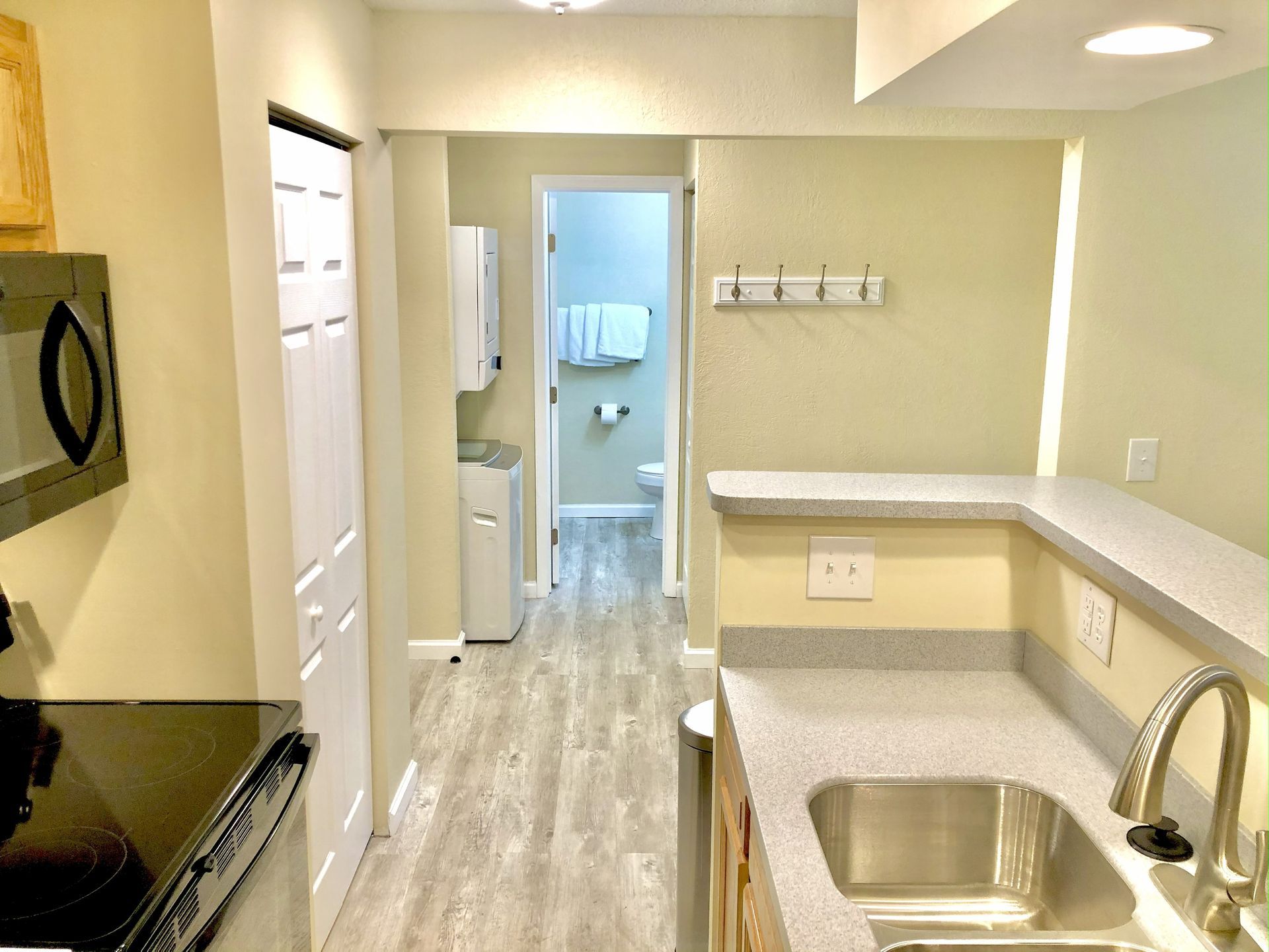 Kitchen with light gray countertops, stainless steel sink, and doorway to hallway with bathroom and laundry.