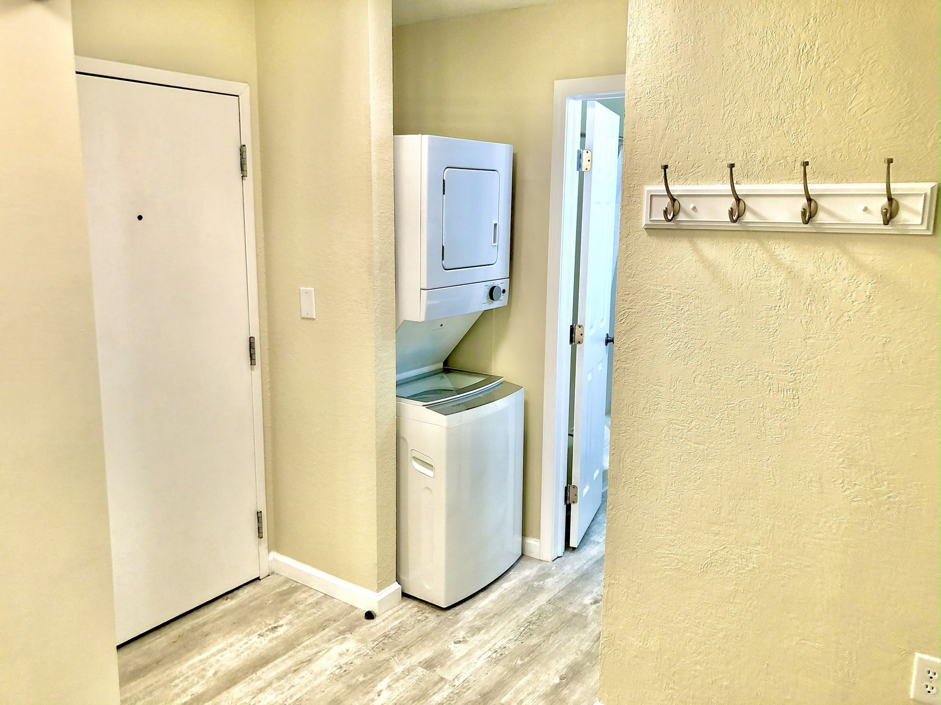 Hallway with stacked washer and dryer, white doors, coat rack.