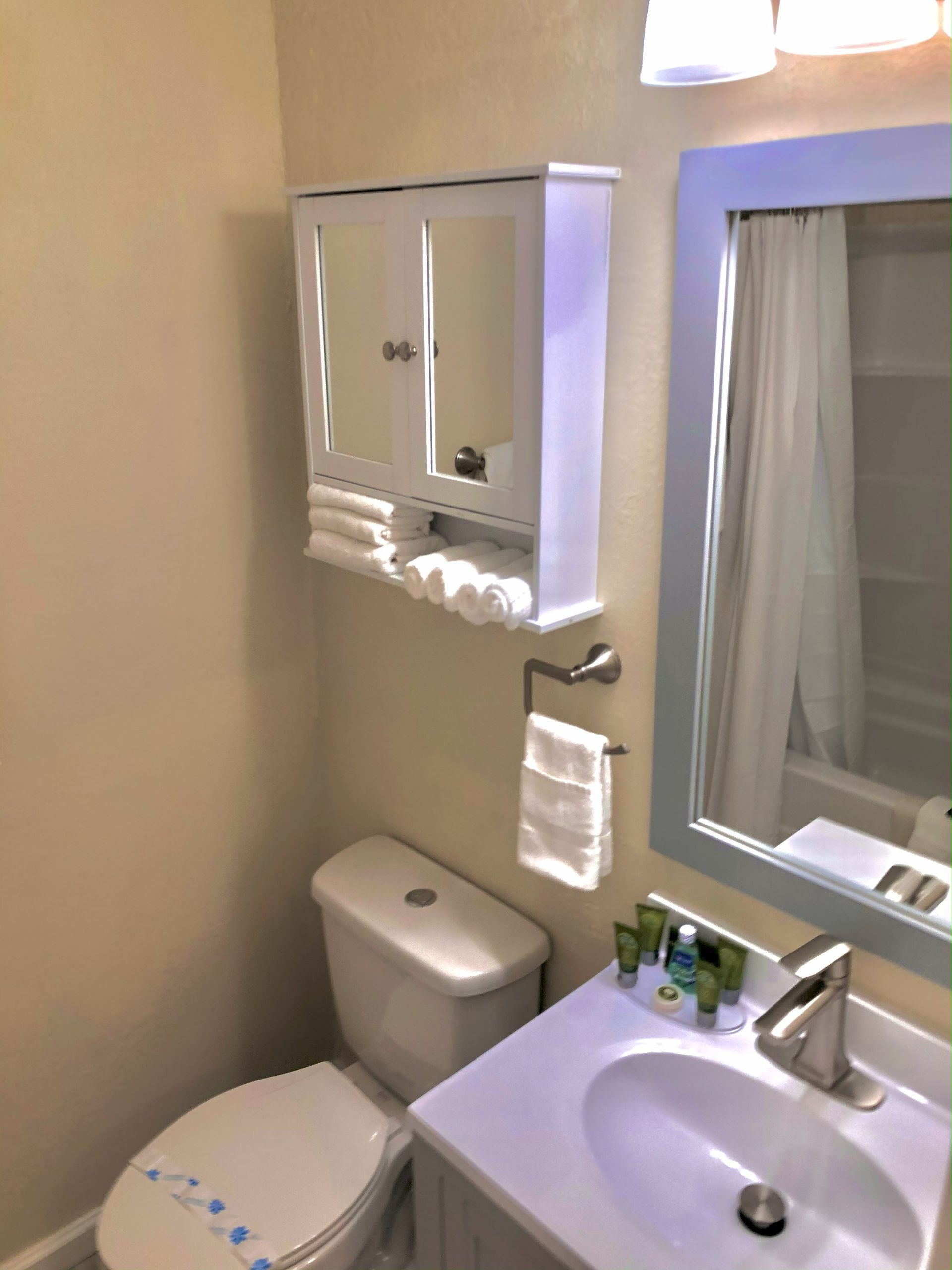 Bathroom with a white toilet, vanity, and medicine cabinet with towels; light blue accents.