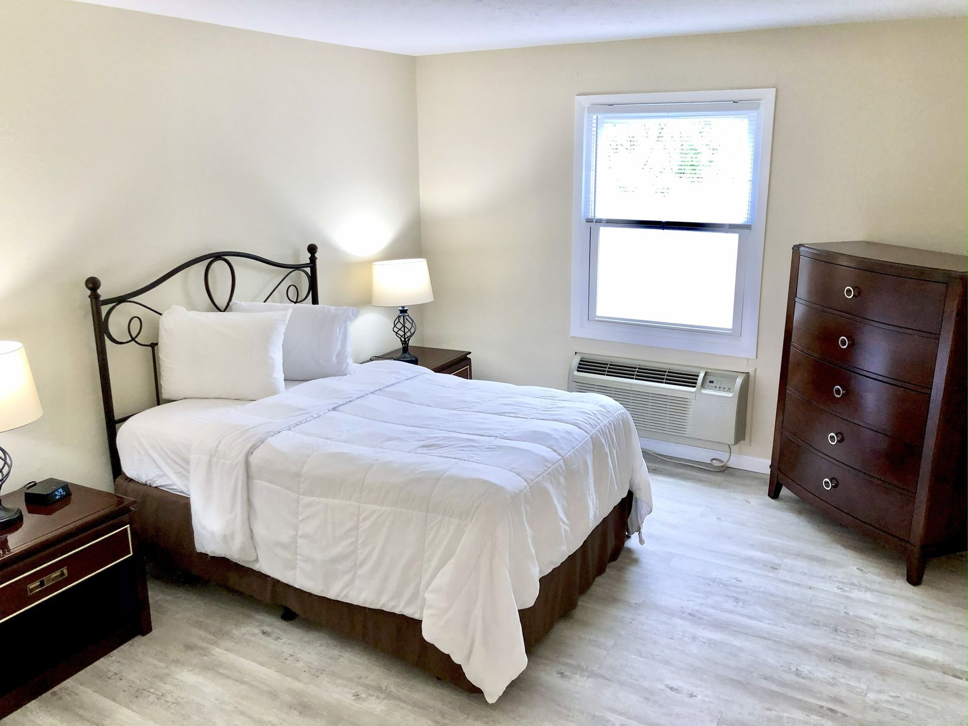 Bedroom with a double bed, nightstands with lamps, dresser, and a window. Light wood flooring and neutral walls.