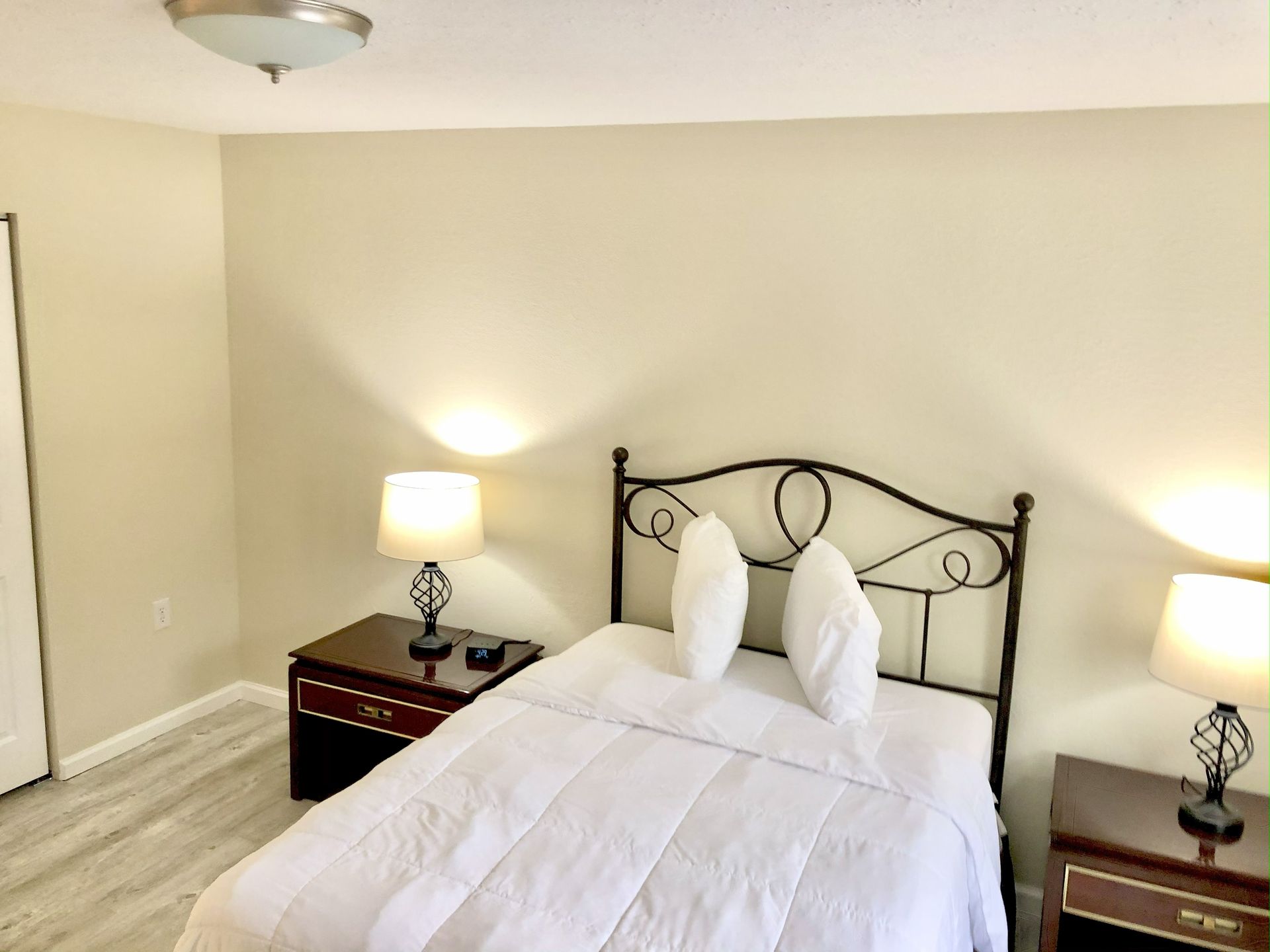 Bedroom with bed, two nightstands, lamps, and a closet. Light-colored walls and flooring.