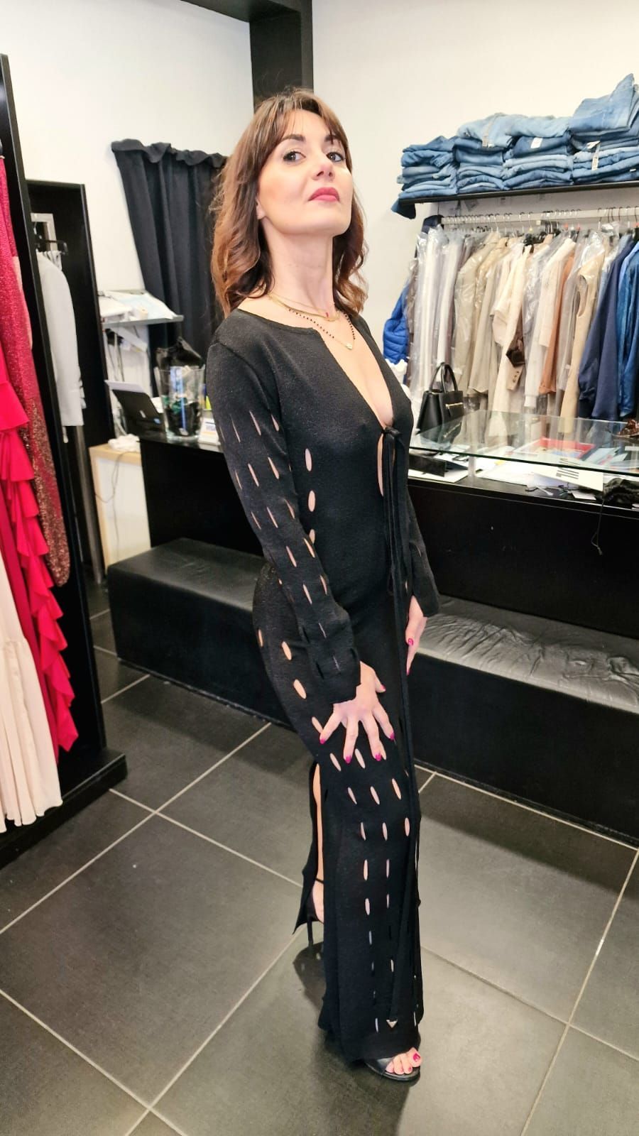 Una donna posa in una boutique, indossando un completo nero con pantaloni allacciati e tacchi alti.
