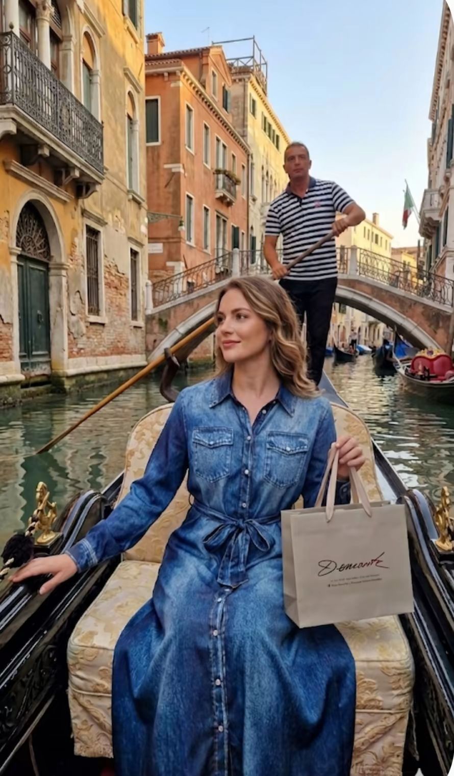 Una donna in abito blu su una gondola a Venezia, con un uomo in piedi dietro di lei sul canale.