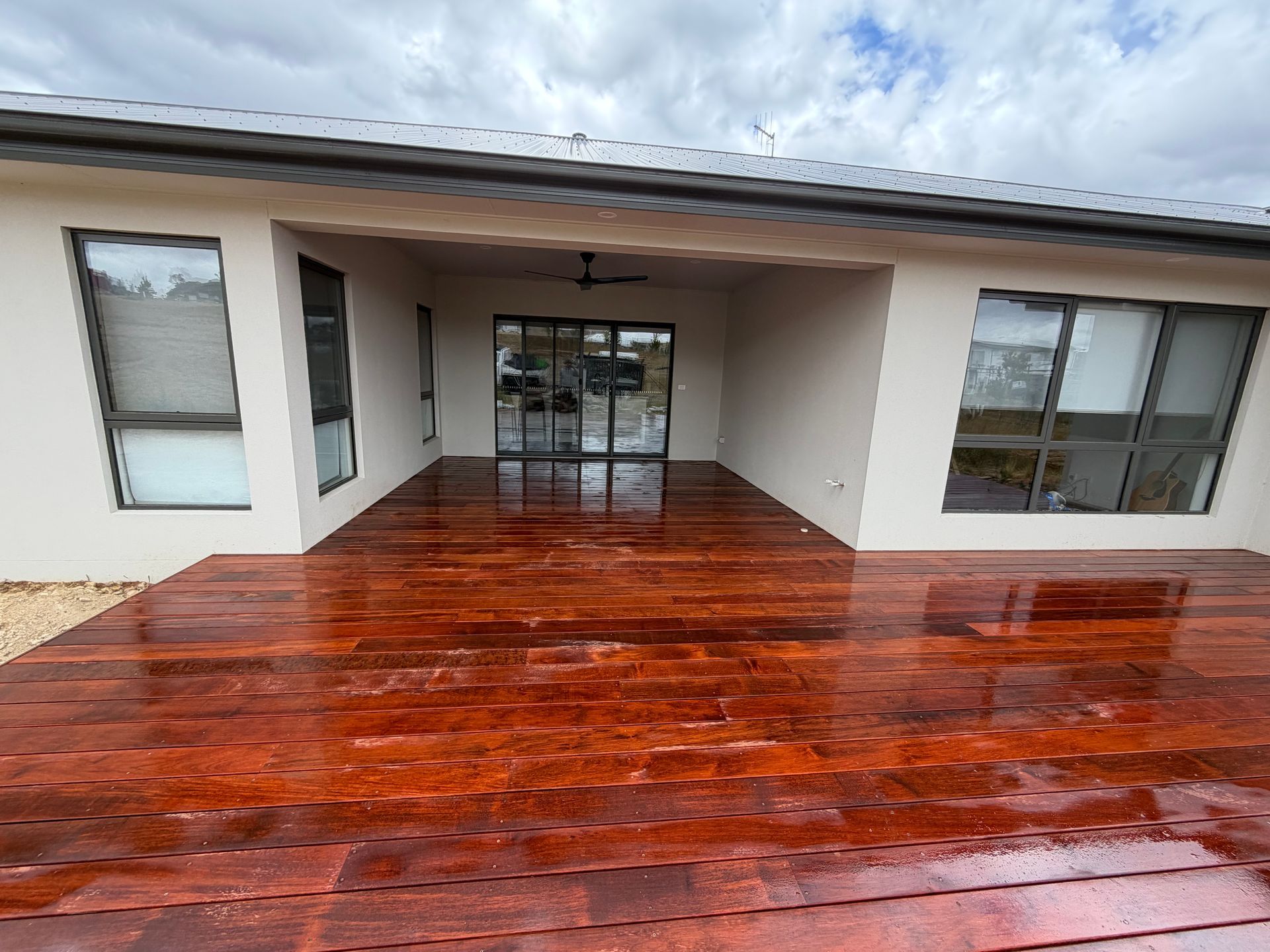 Wooden deck under a covered patio reflecting the sky. Dark wood planks, light walls, and windows. — Straight up Building Projects in Holt, ACT