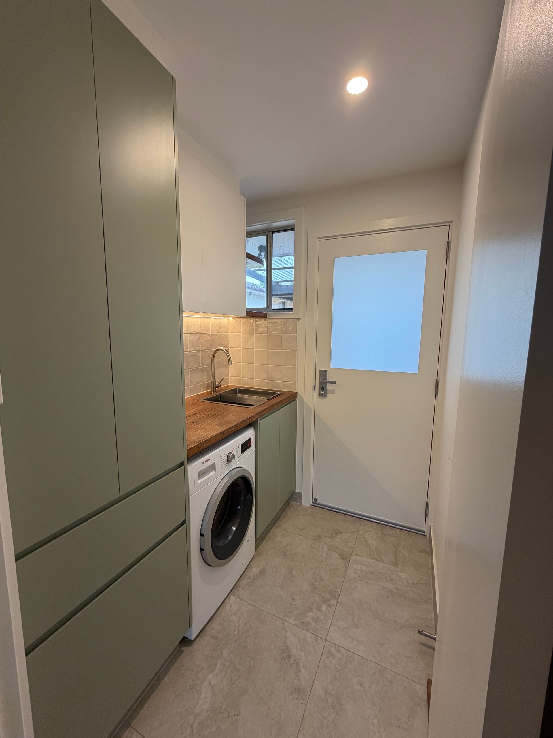 Laundry room with green cabinets, washing machine, sink, and white door. — Straight up Building Projects in Holt, ACT