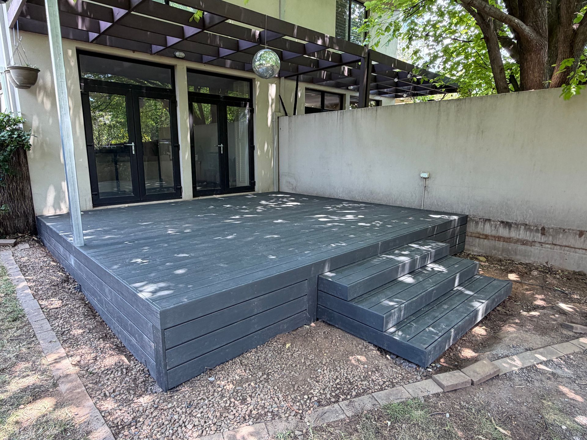 Outdoor composite deck with steps, gray boards, gravel ground, and building with black doors. — Straight up Building Projects in Narrabundah, ACT