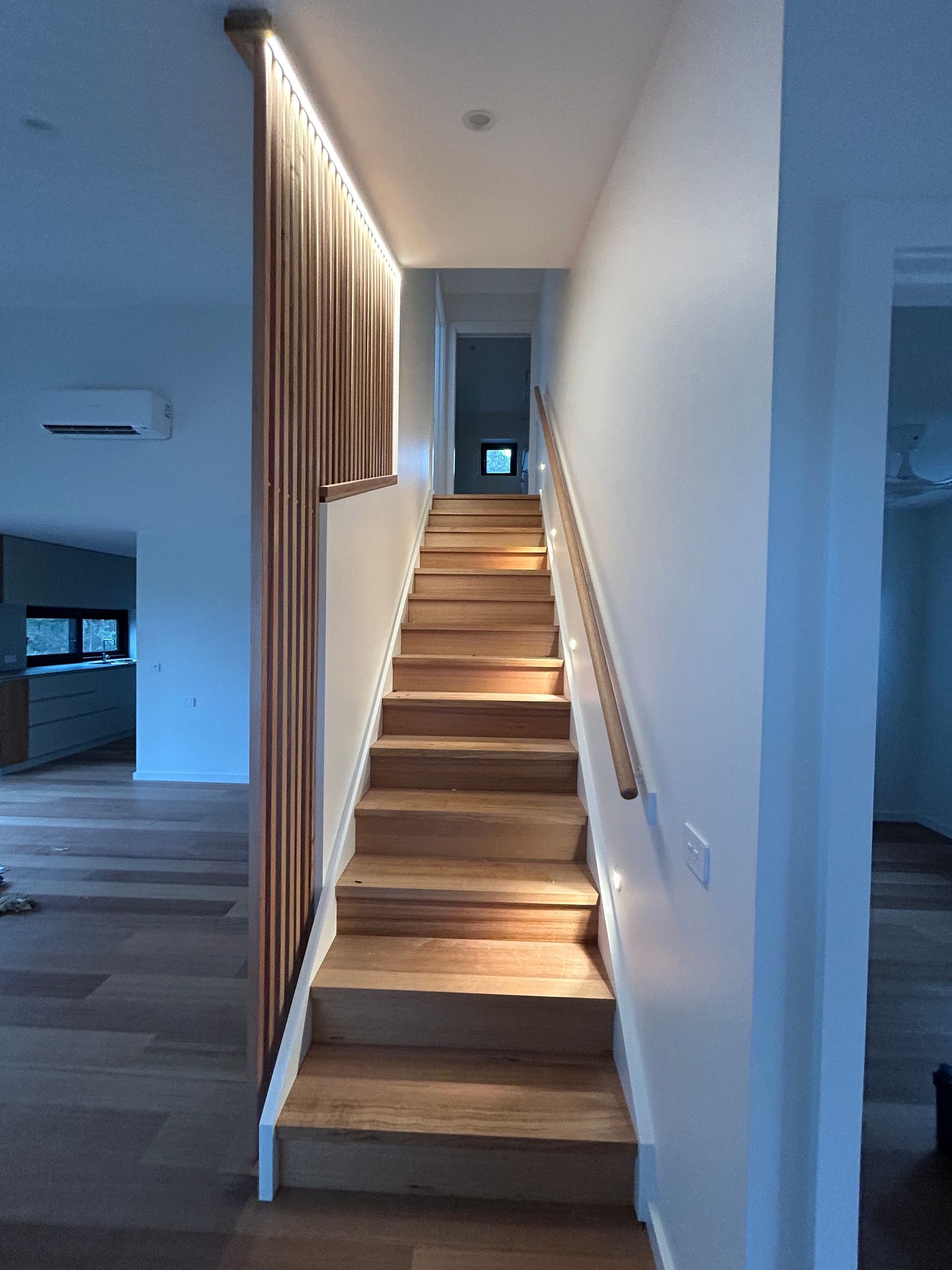 Wooden staircase with handrail, lit by overhead lighting. Wall on the right and wooden slat barrier on the left. — Straight up Building Projects in Holt, ACT