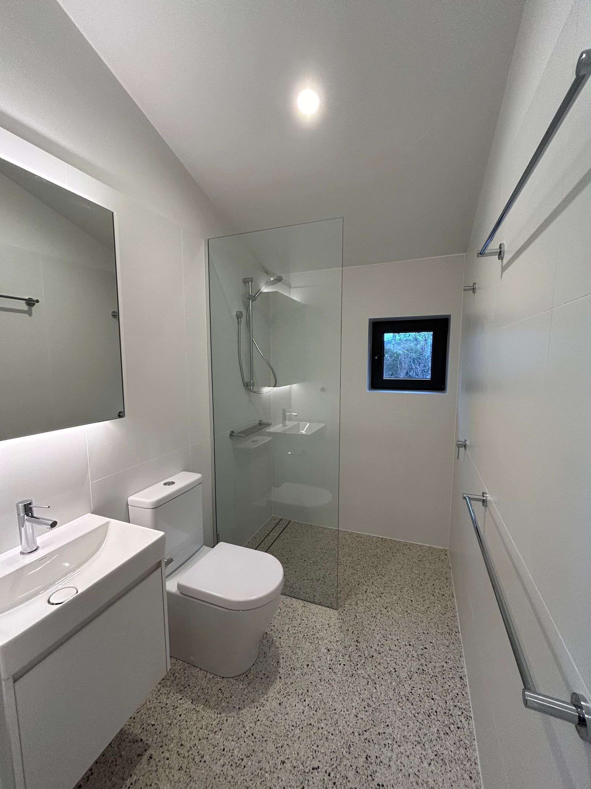 Modern, white bathroom with a shower, toilet, and sink. Pebble floor, small window, and towel bars. — Straight up Building Projects in Holt, ACT