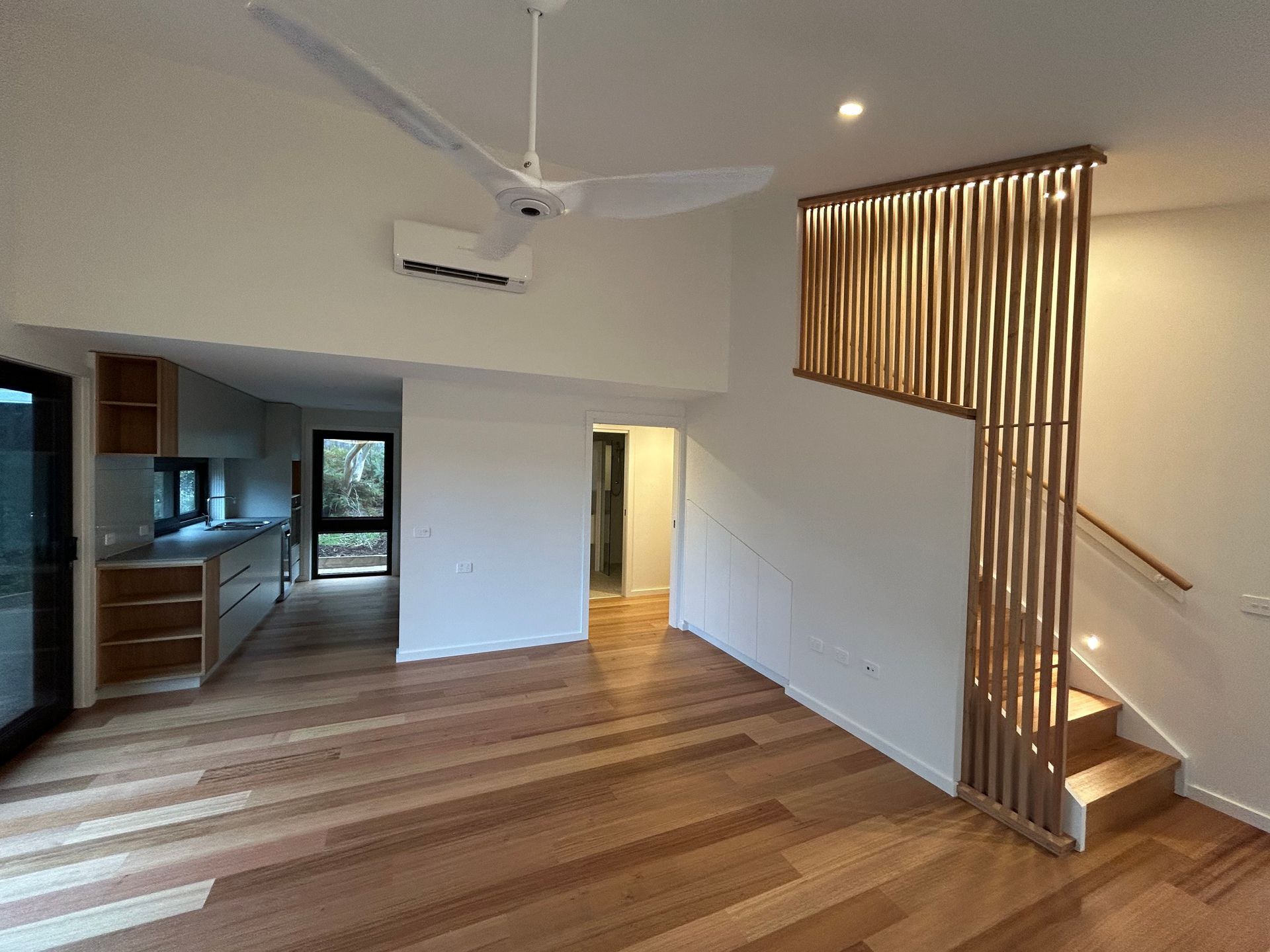 Interior view: Open-plan living space with wooden floors, staircase, kitchen, and decorative wooden panel. — Straight up Building Projects in Holt, ACT