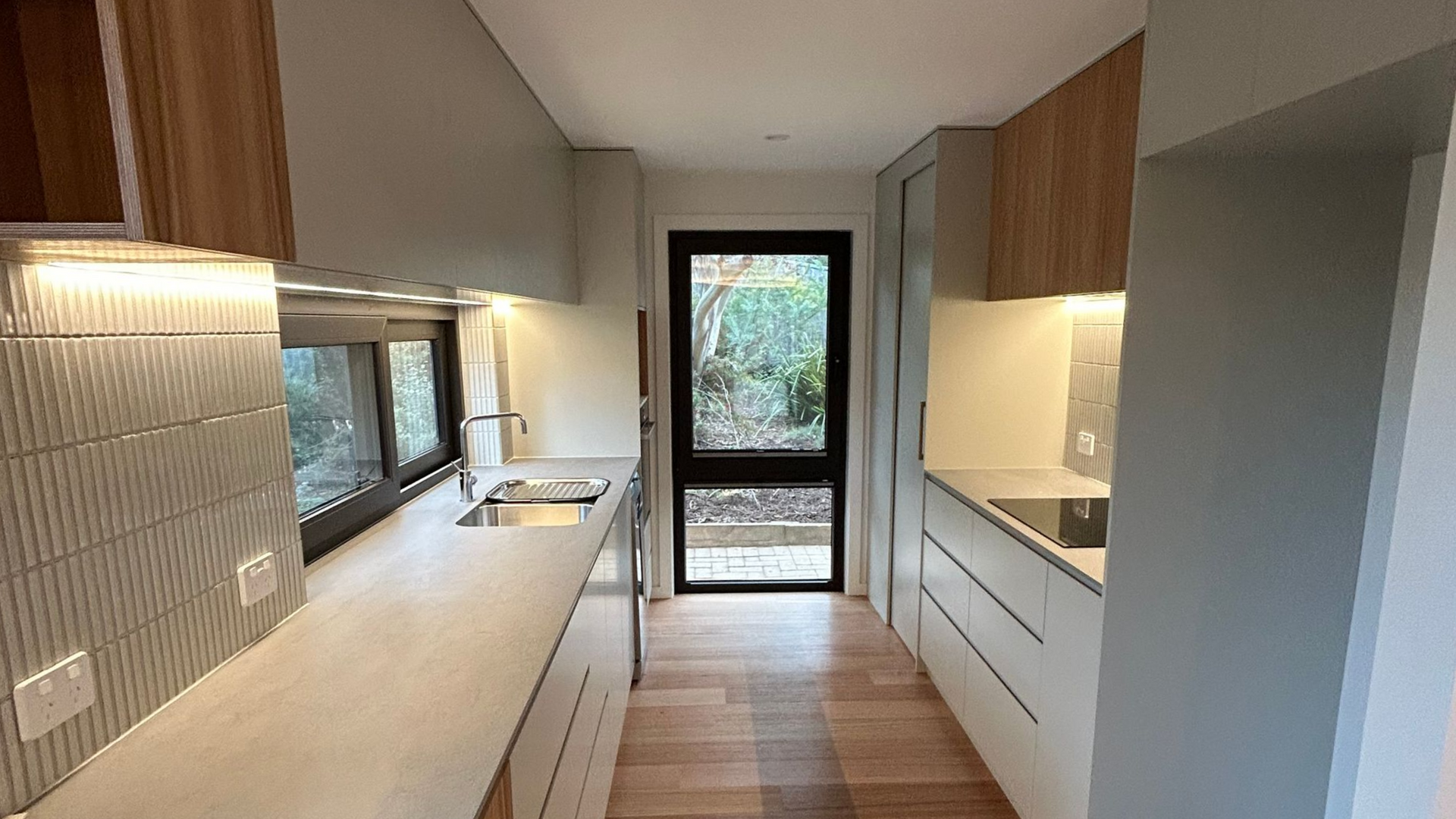 Modern kitchen with light wood cabinets, light countertops, and a black-framed door. — Straight up Building Projects in Weston Creek, ACT