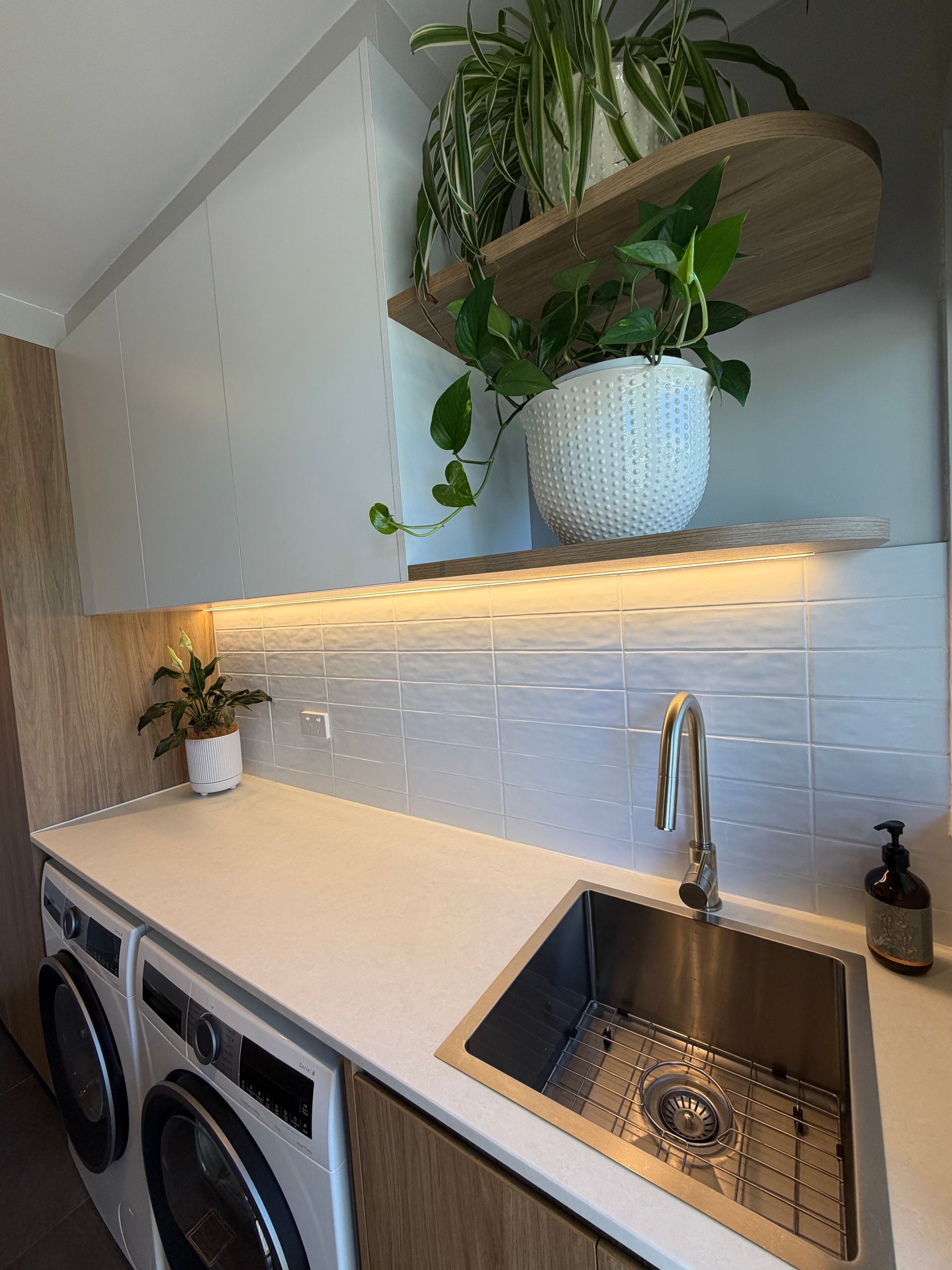 Modern laundry room with white countertop, sink, and decorative shelving with plants. — Straight up Building Projects in Holt, ACT