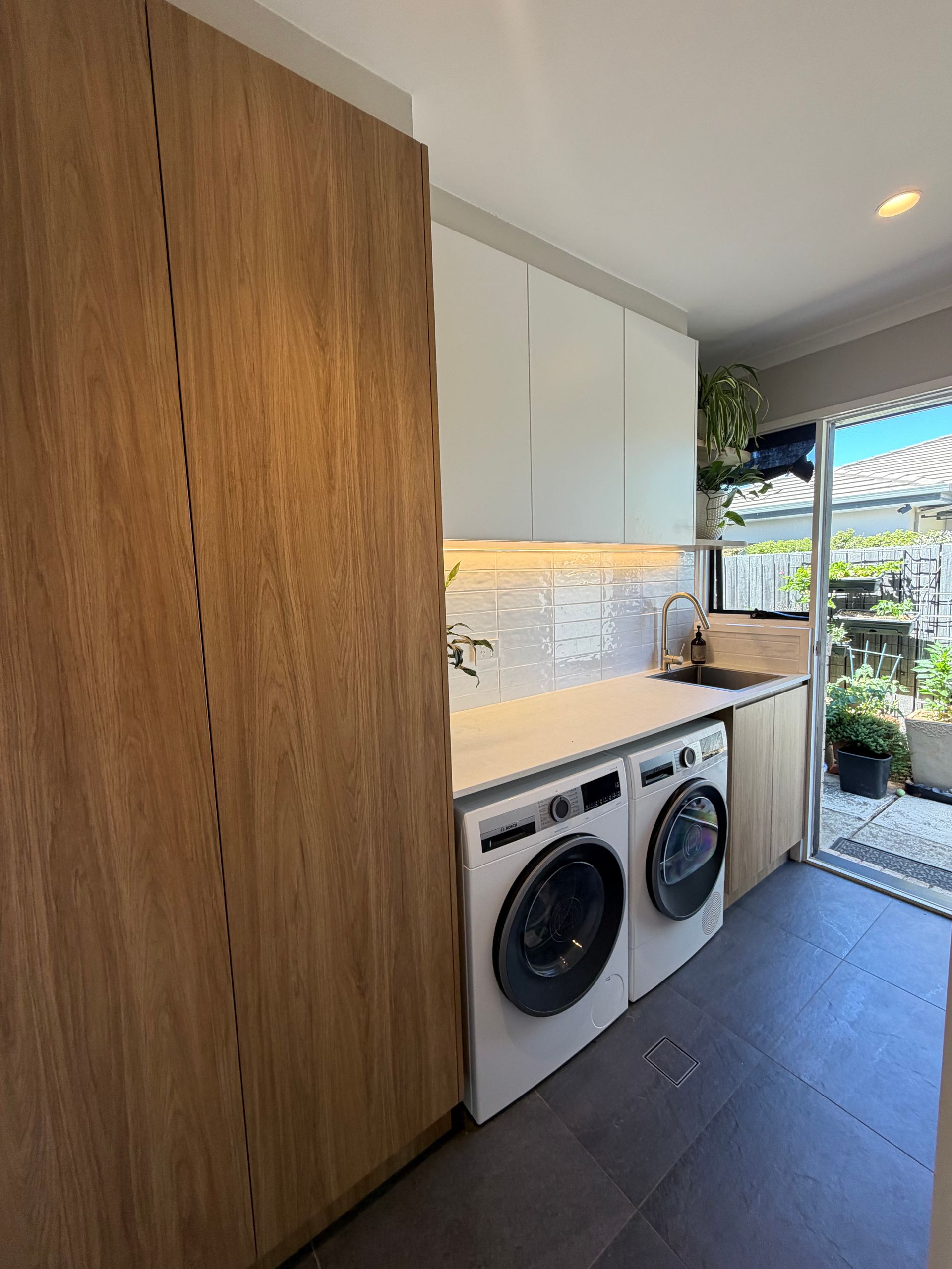 Laundry room with a washing machine, dryer, cabinets, and a view to a patio. — Straight up Building Projects in Holt, ACT