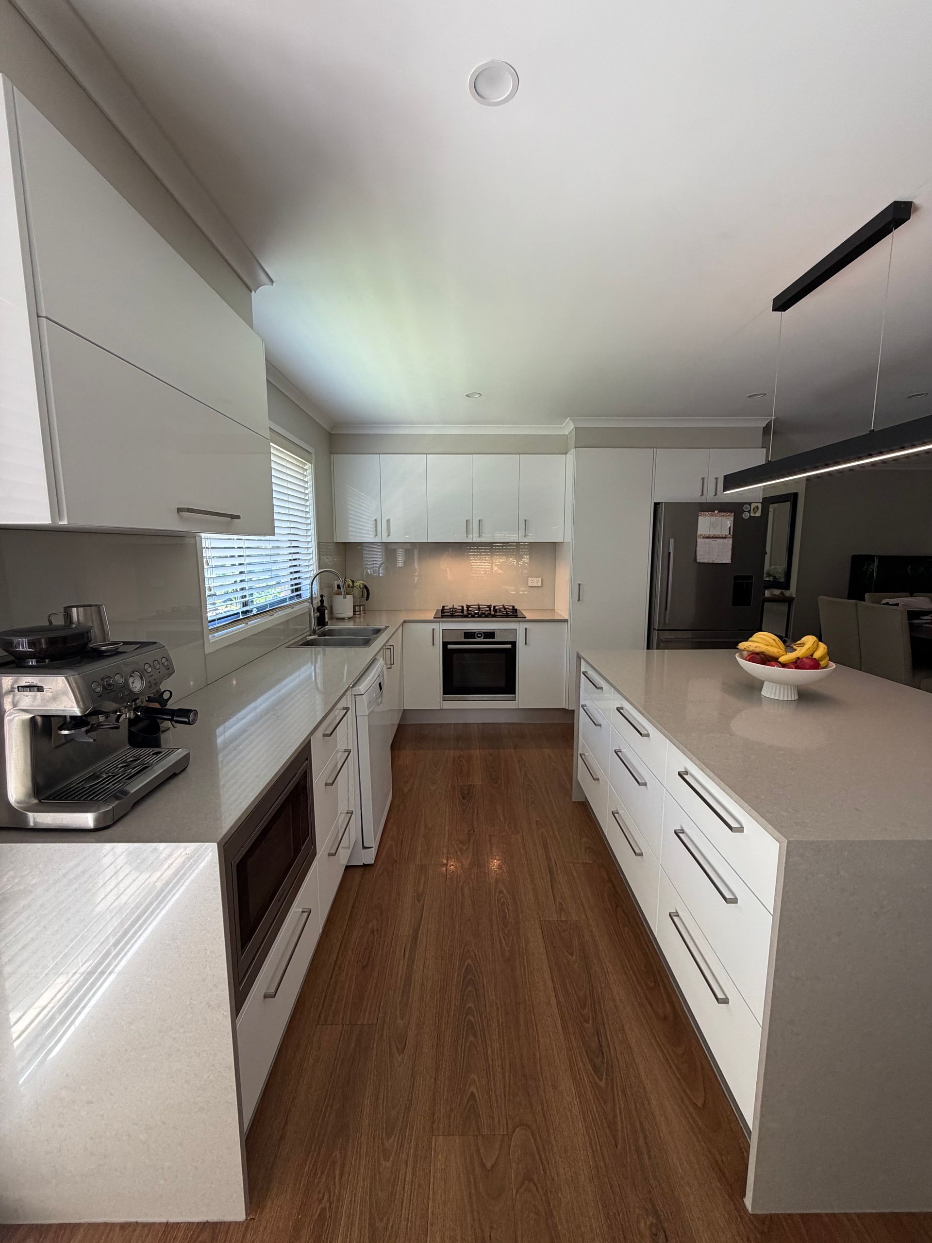 Modern white kitchen with wooden floors and a large island. — Straight up Building Projects in Holt, ACT