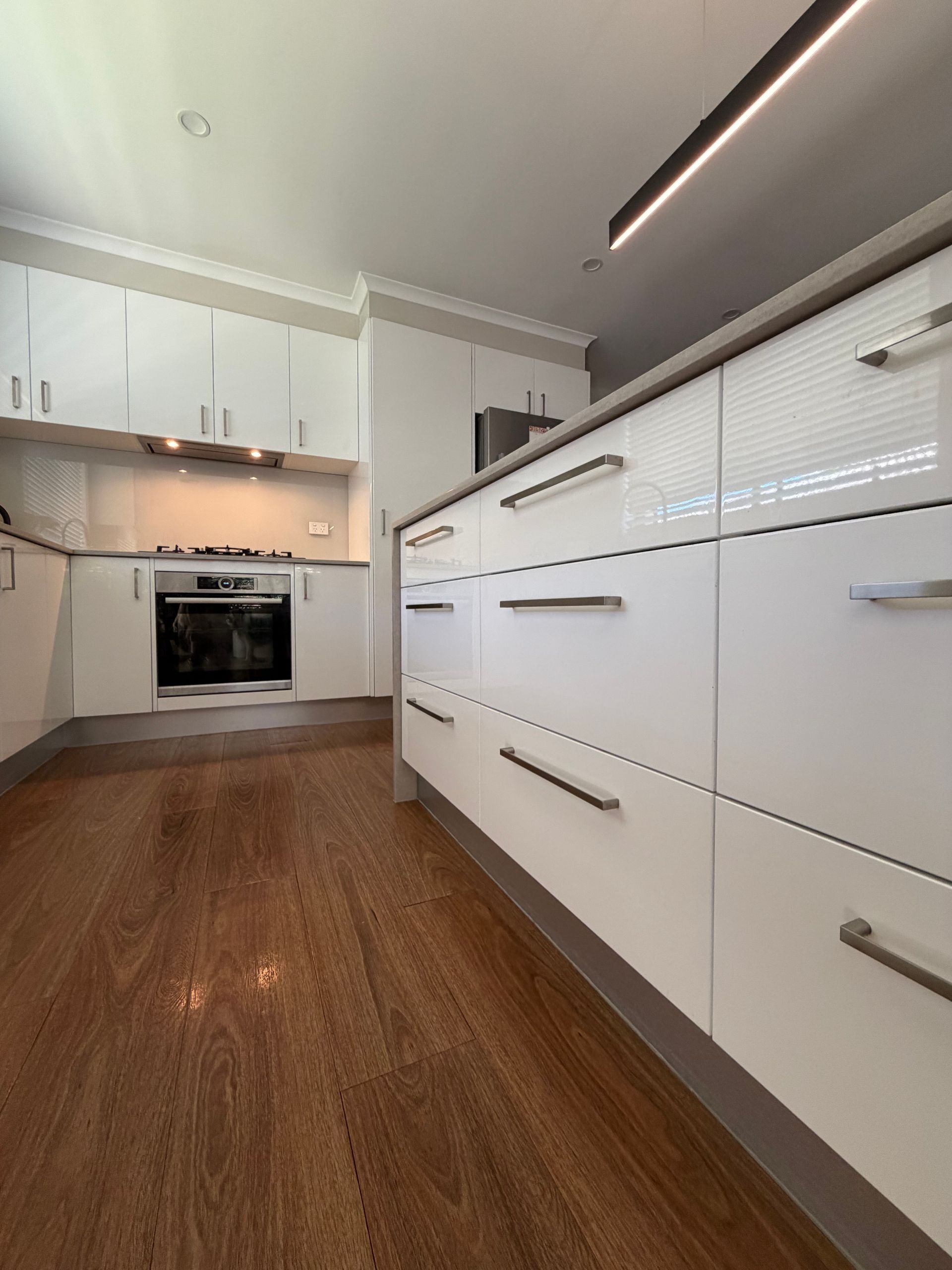 White kitchen with glossy cabinets, stainless steel hardware, and wooden flooring. — Straight up Building Projects in Holt, ACT