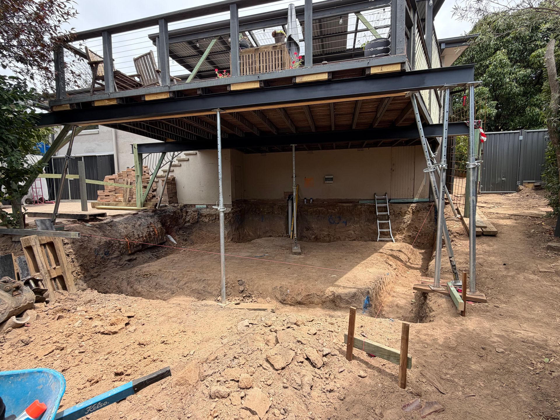Construction site: Elevated deck supported by steel beams. Ground-level excavation with scaffolding and support posts. — Straight up Building Projects in Holt, ACT