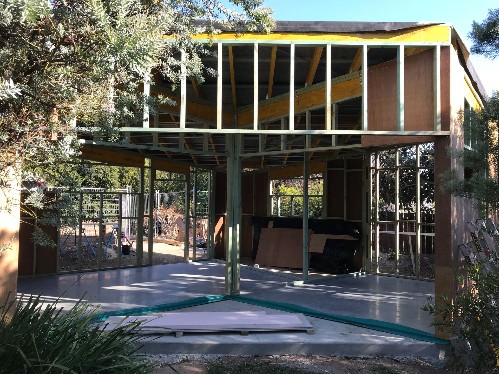 An open-frame structure of a room under construction with wooden wall studs, a gray concrete floor, and trees outside — Straight up Building Projects in Ainslie, ACT