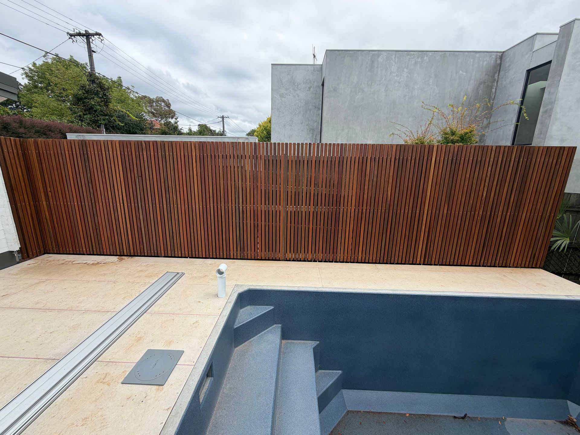 A vertical wooden slat privacy fence bordering a tiled pool deck with stairs leading into a dark blue swimming pool — Straight up Building Projects in Holt, ACT