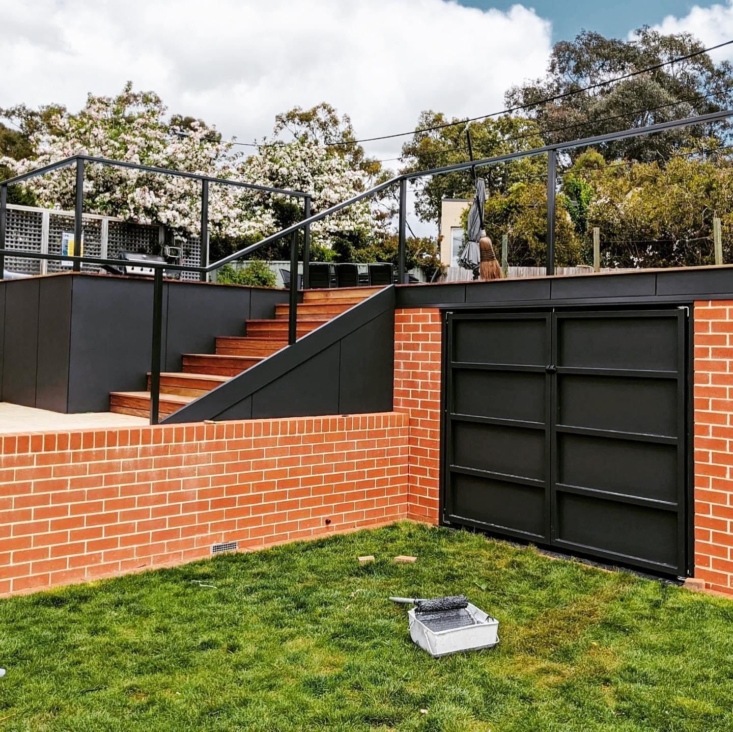 Exterior view: brick wall, black gate, stairs to a deck, and green grass. — Straight up Building Projects in Holt, ACT