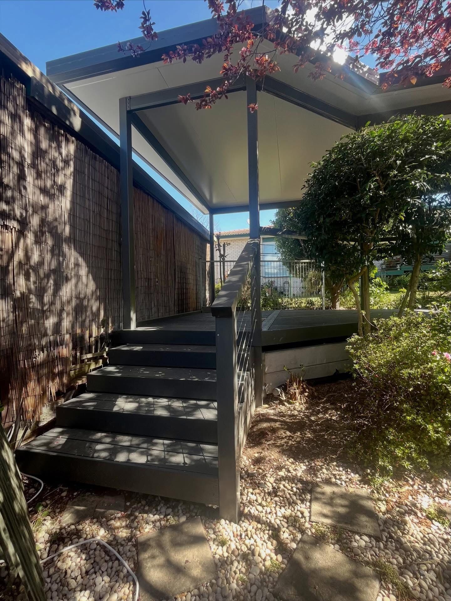 Exterior view of steps leading to a covered porch with a dark gray frame, surrounded by greenery. — Straight up Building Projects in Holt, ACT