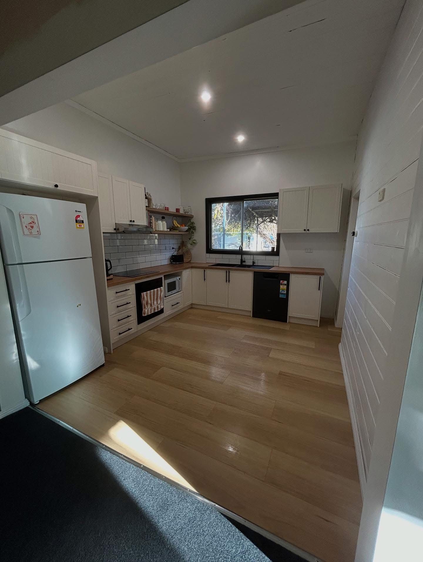 Kitchen with white cabinets, wooden floor, appliances, and a window. — Straight up Building Projects in Holt, ACT