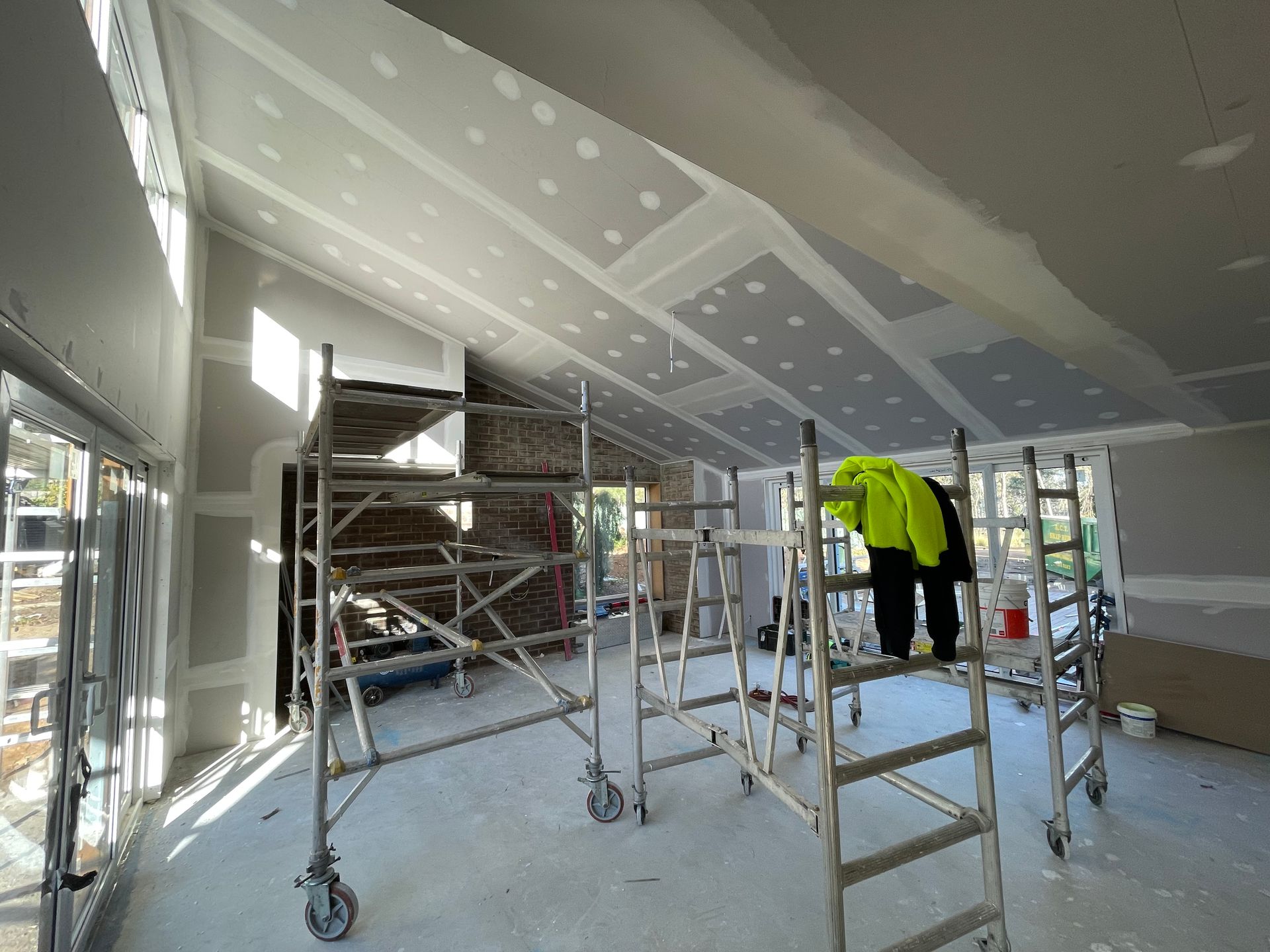 Construction site interior: Scaffolding, drywall, and a worker in a neon vest, with an unfinished sloped ceiling. — Straight up Building Projects in Holt, ACT