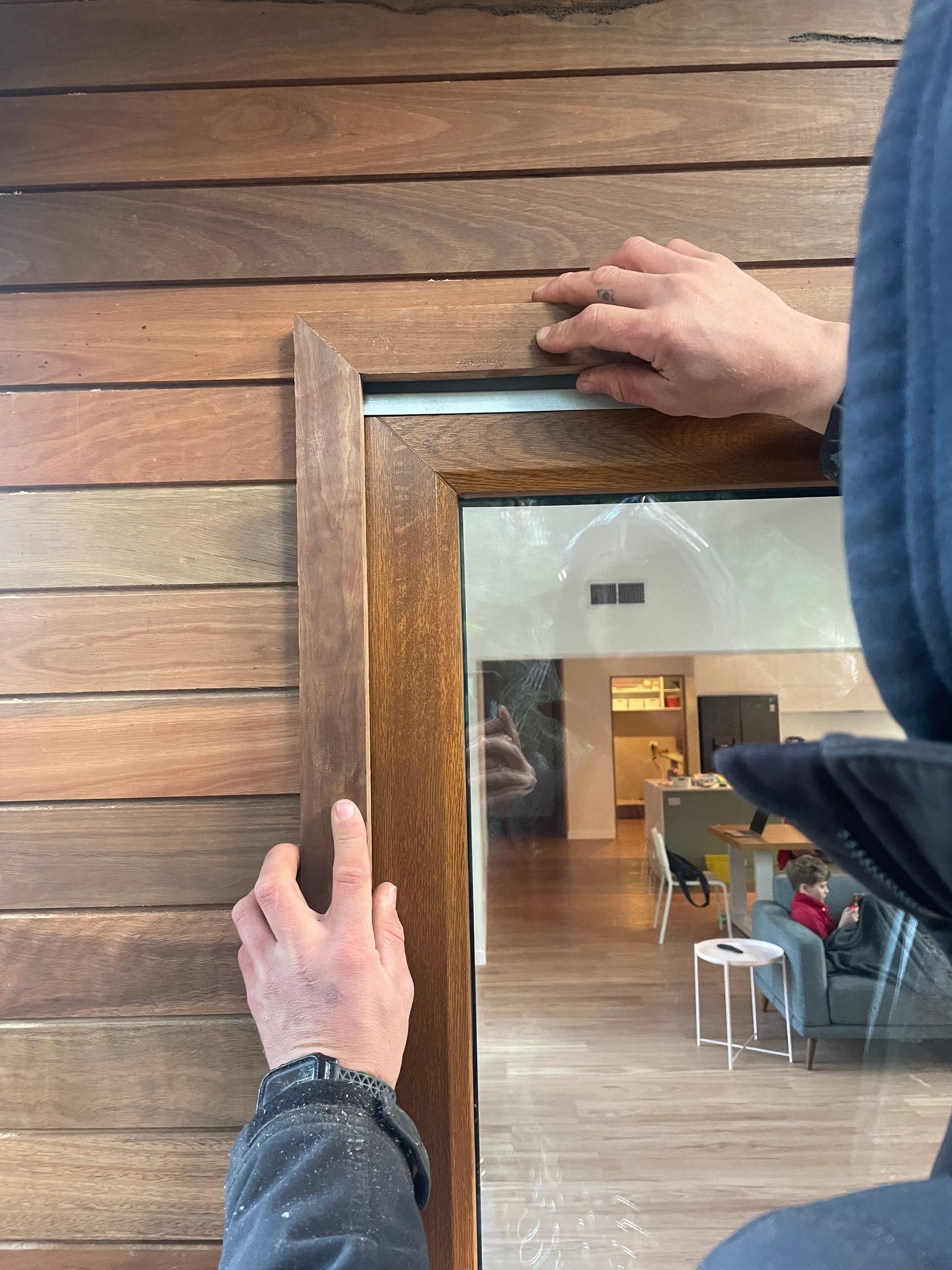 Person installing wooden trim around a doorway. The trim is a darker brown, and the wall is composed of horizontal wooden planks. — Straight up Building Projects in Holt, ACT