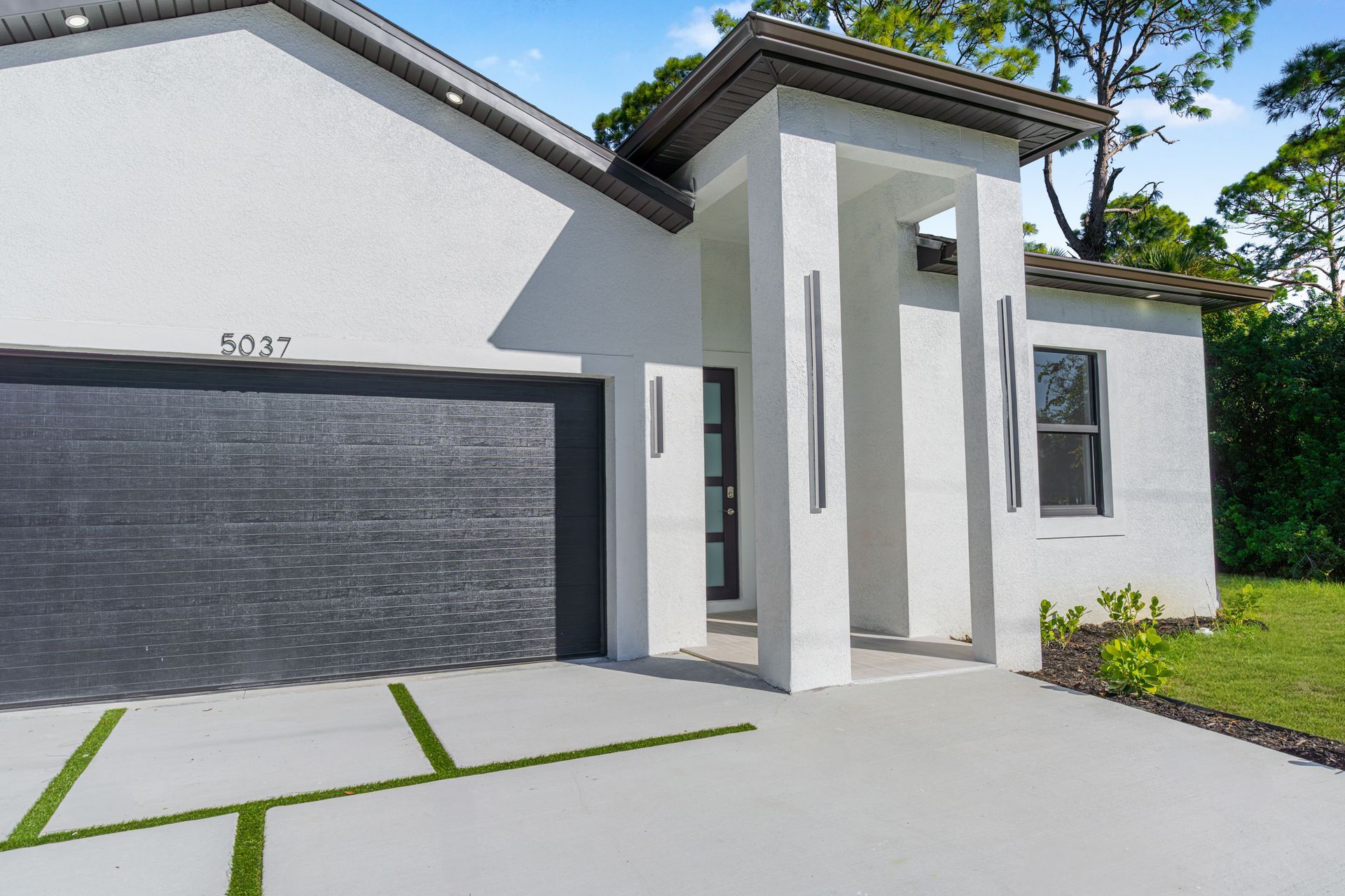 Modern white house with a black garage door and an entryway. Green lawn.