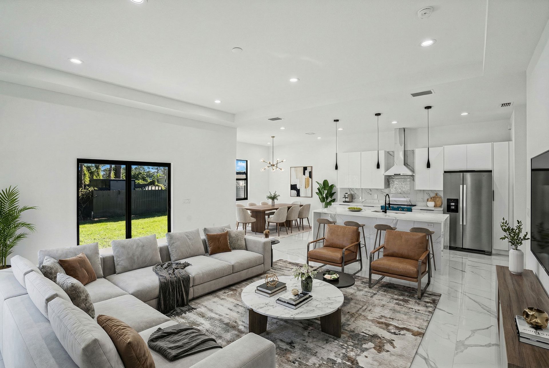 Modern open-concept living space with a sectional sofa, kitchen island, and dining area, all in a bright, white color scheme.