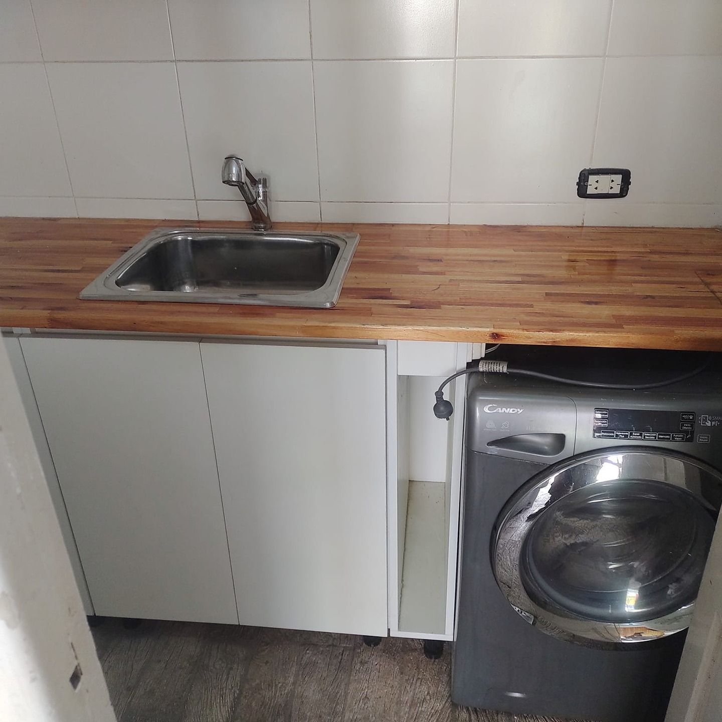 Área de lavado con fregadero, gabinetes, encimera de madera y lavadora.