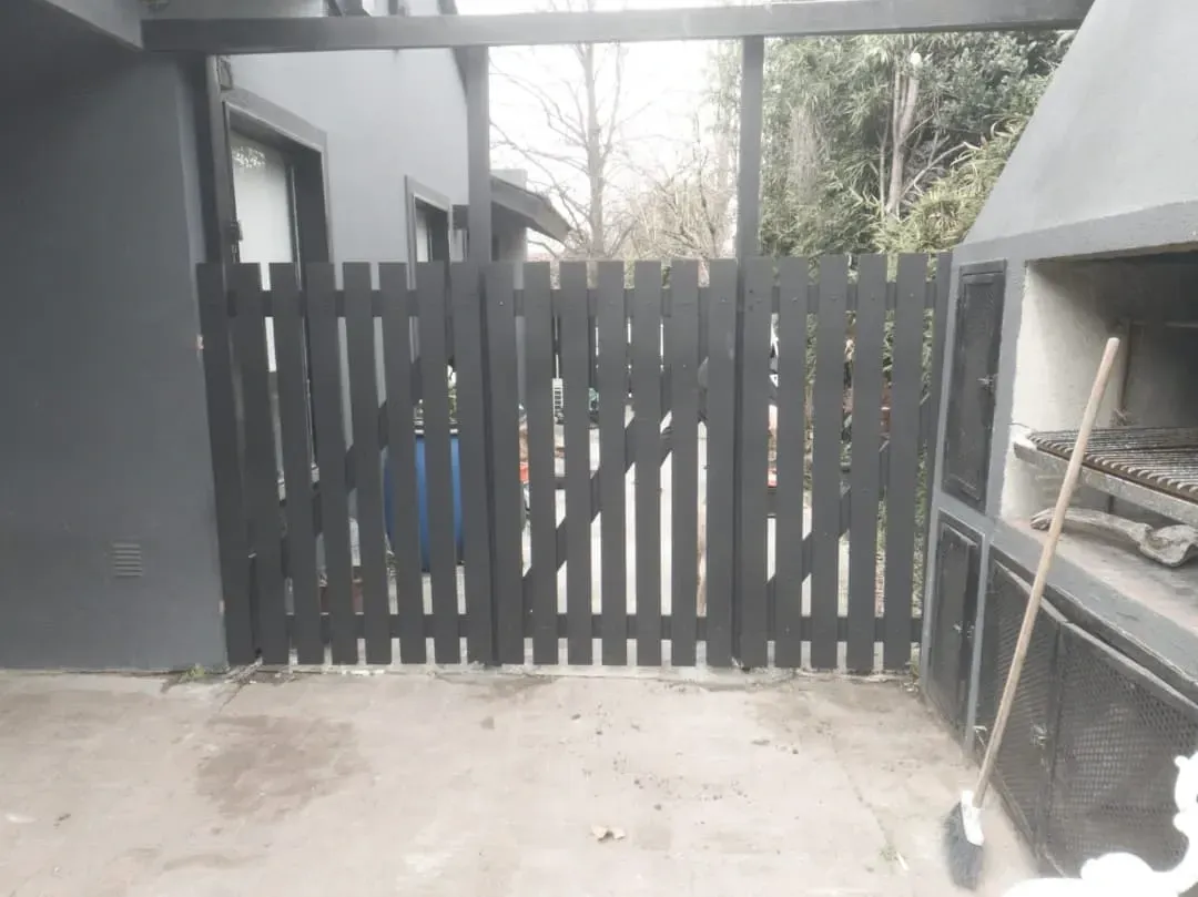 Valla de madera negra con barbacoa a la derecha y edificio a la izquierda.