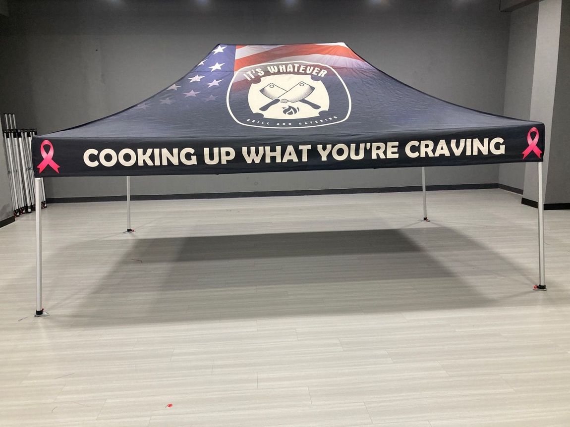 Black canopy tent with pink ribbon logos and “COOKING UP WHAT YOU’RE CRAVING” text in an empty room