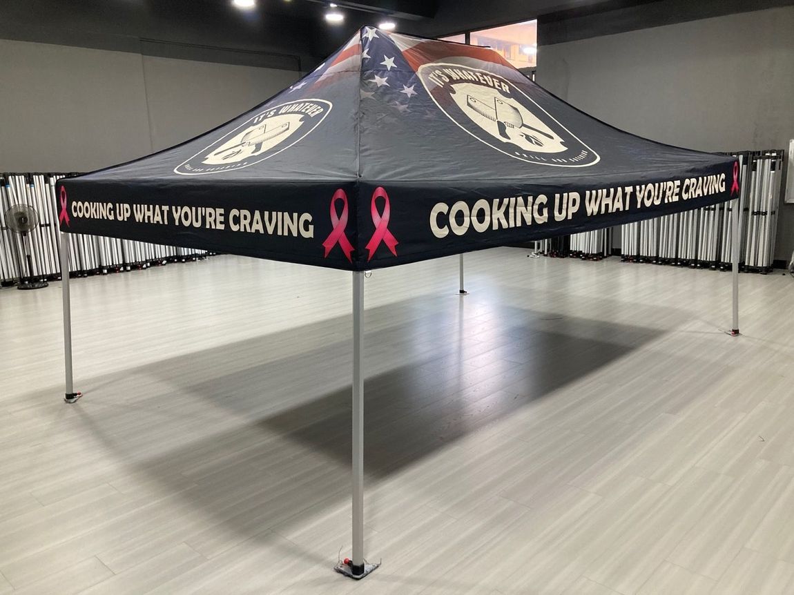 Black promotional canopy tent with pink ribbon graphics and “Cooking Up What You Craving” text indoors
