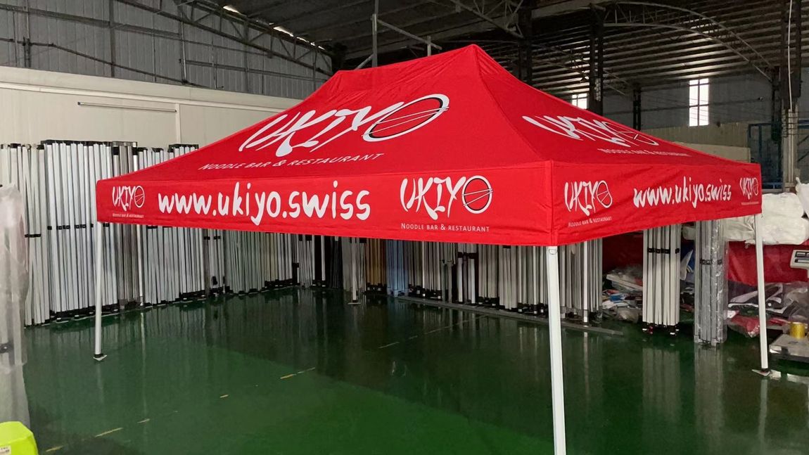 Red promotional canopy tent with white text set up indoors in a warehouse-like space.