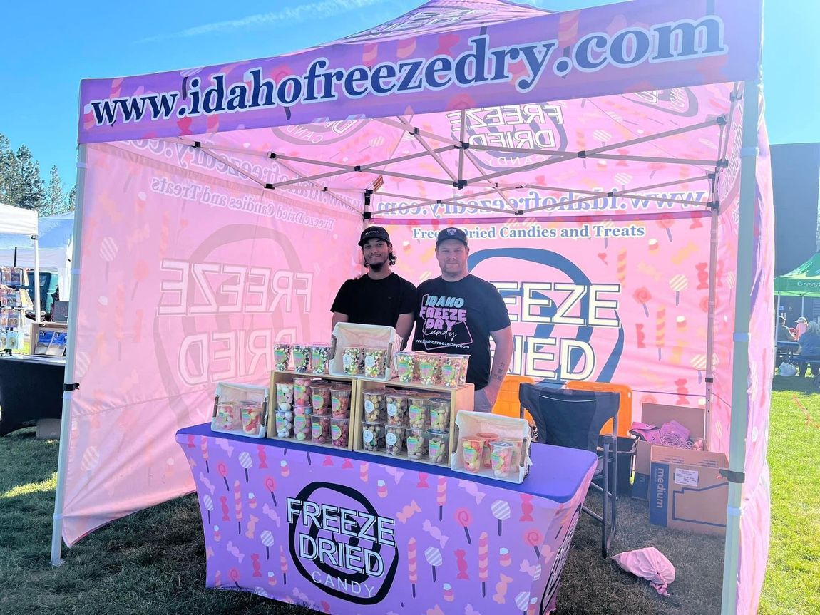 Pink vendor booth with two people behind a table displaying rows of canned drinks and branded signage