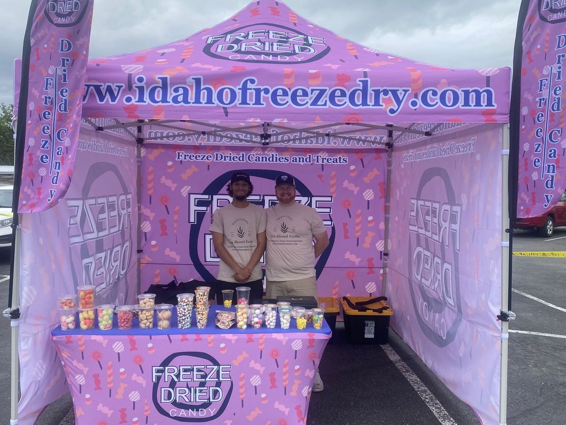 Pink Idaho Freeze Dry booth with two staff behind a display table of frozen treats at an outdoor event