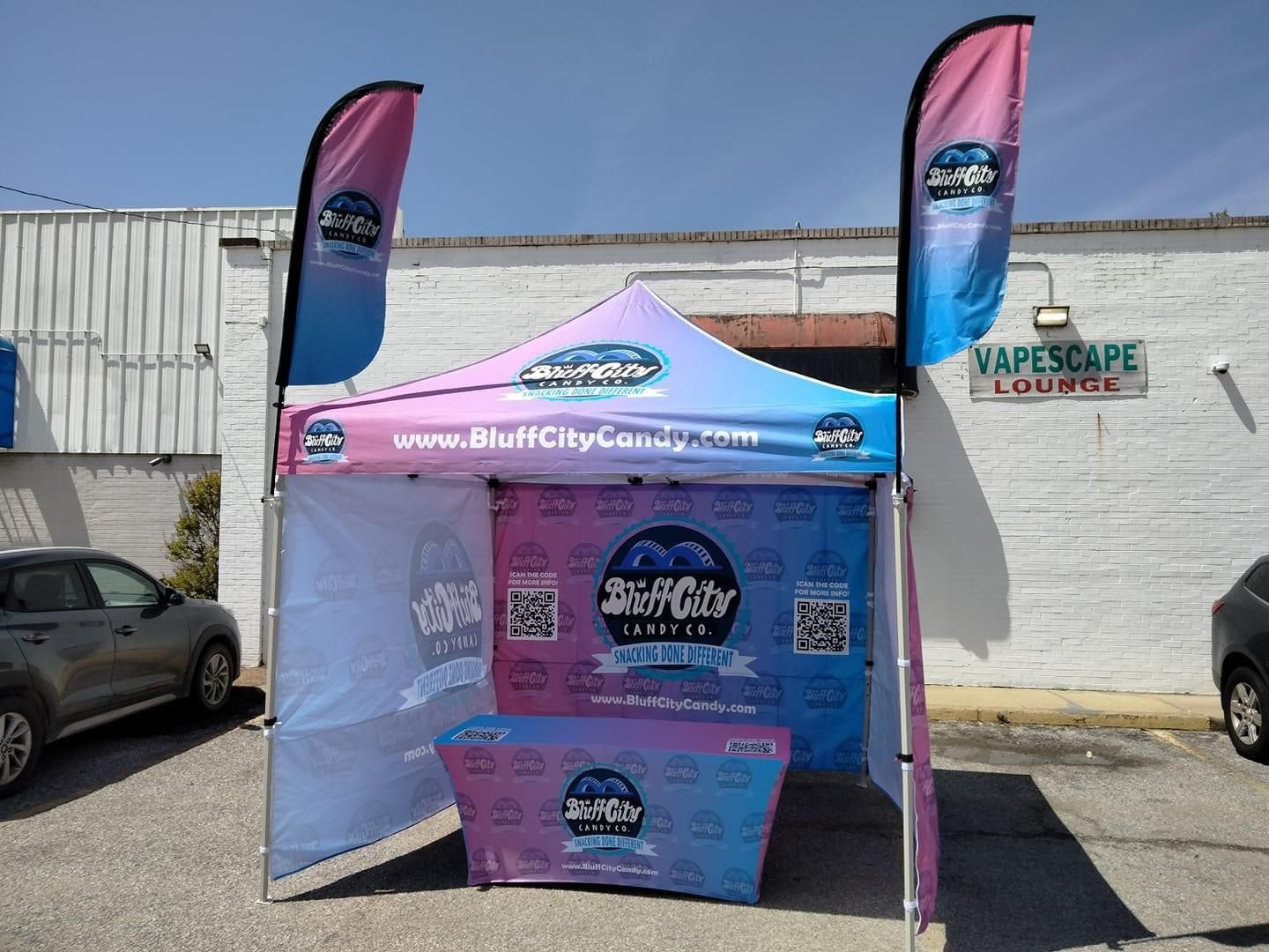 A tent with a table in front of a building that says vapescape lounge