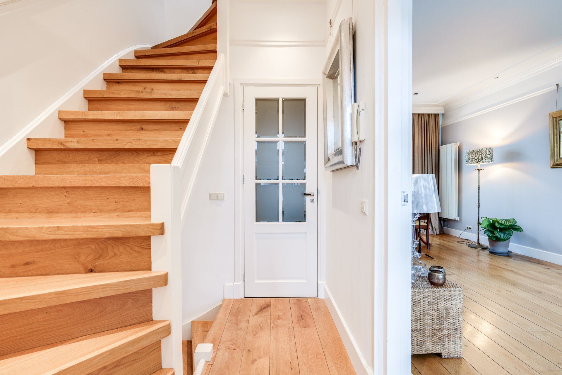 Een gang met een houten trap en een witte deur