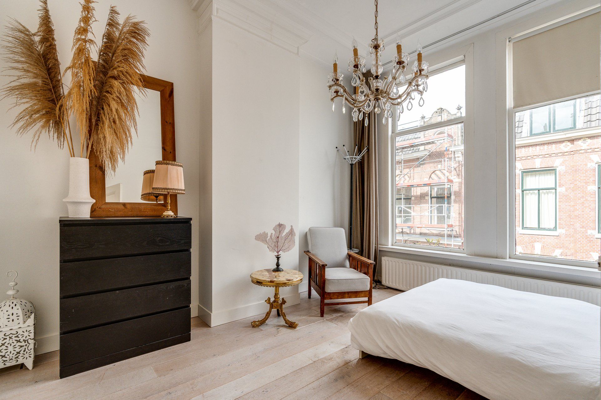 Een slaapkamer met een bed, een ladekast, een stoel en een spiegel.