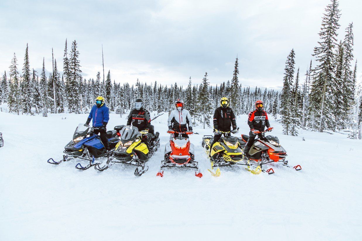 Five people standing on their snowmobiles