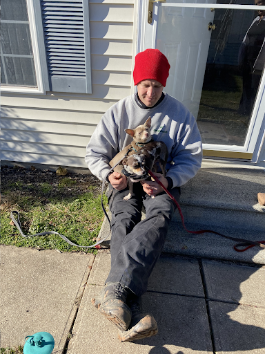 A man is sitting on the steps of a house holding two dogs.