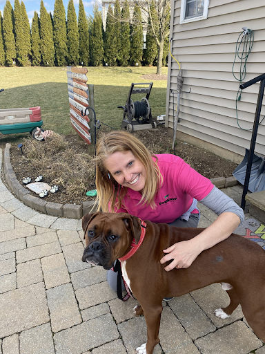 A woman is petting a brown boxer dog on a patio.