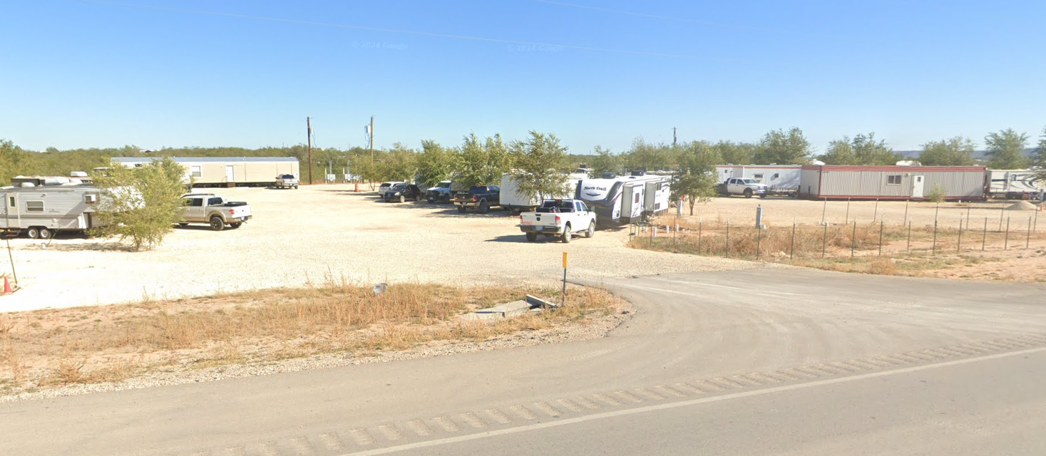 RV park with trailers parked on gravel, under a blue sky.