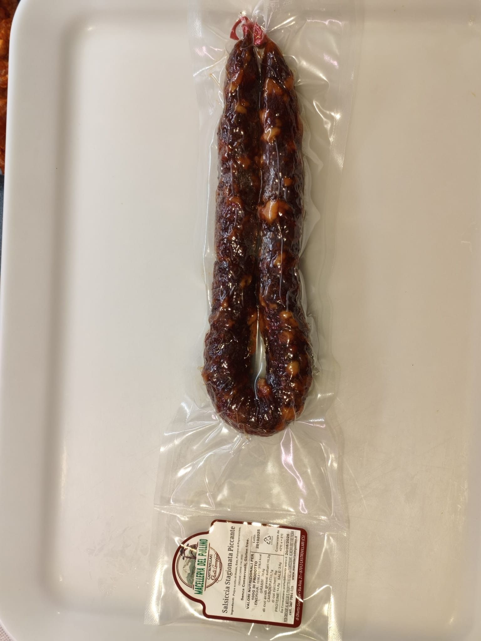 Salumi stagionati appesi su rastrelliere, etichettati con i prezzi, contro una parete piastrellata.