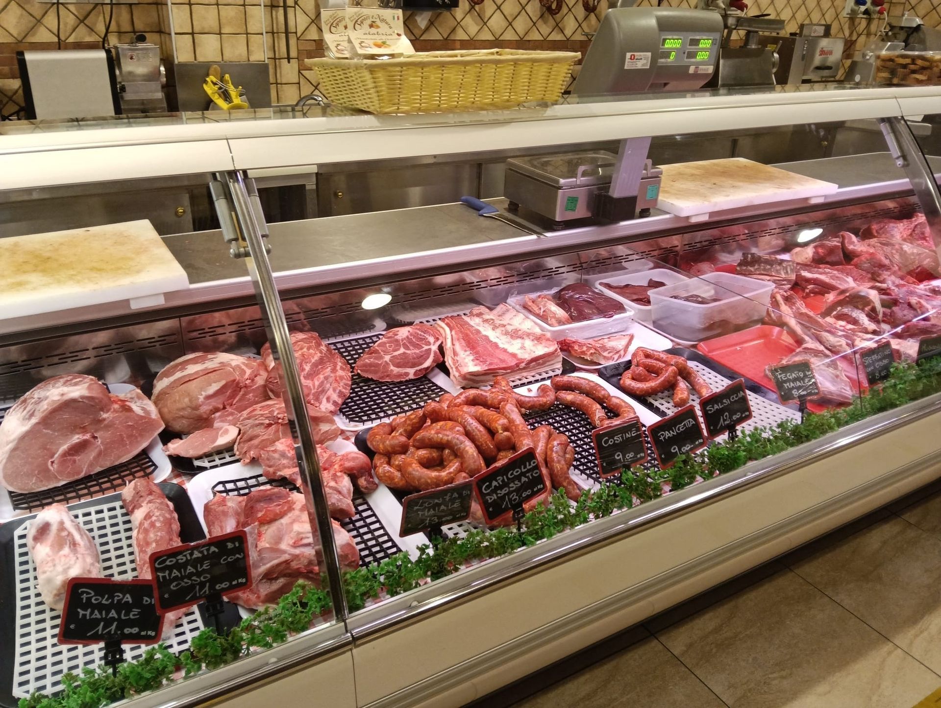 Vetrina per la carne in una macelleria, che espone vari tagli di carne fresca, salsicce ed etichette.