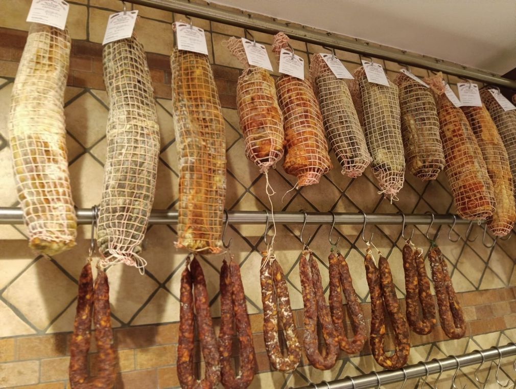 Fila di salumi appesi in un negozio, avvolti in una rete e fissati a una rastrelliera di metallo.