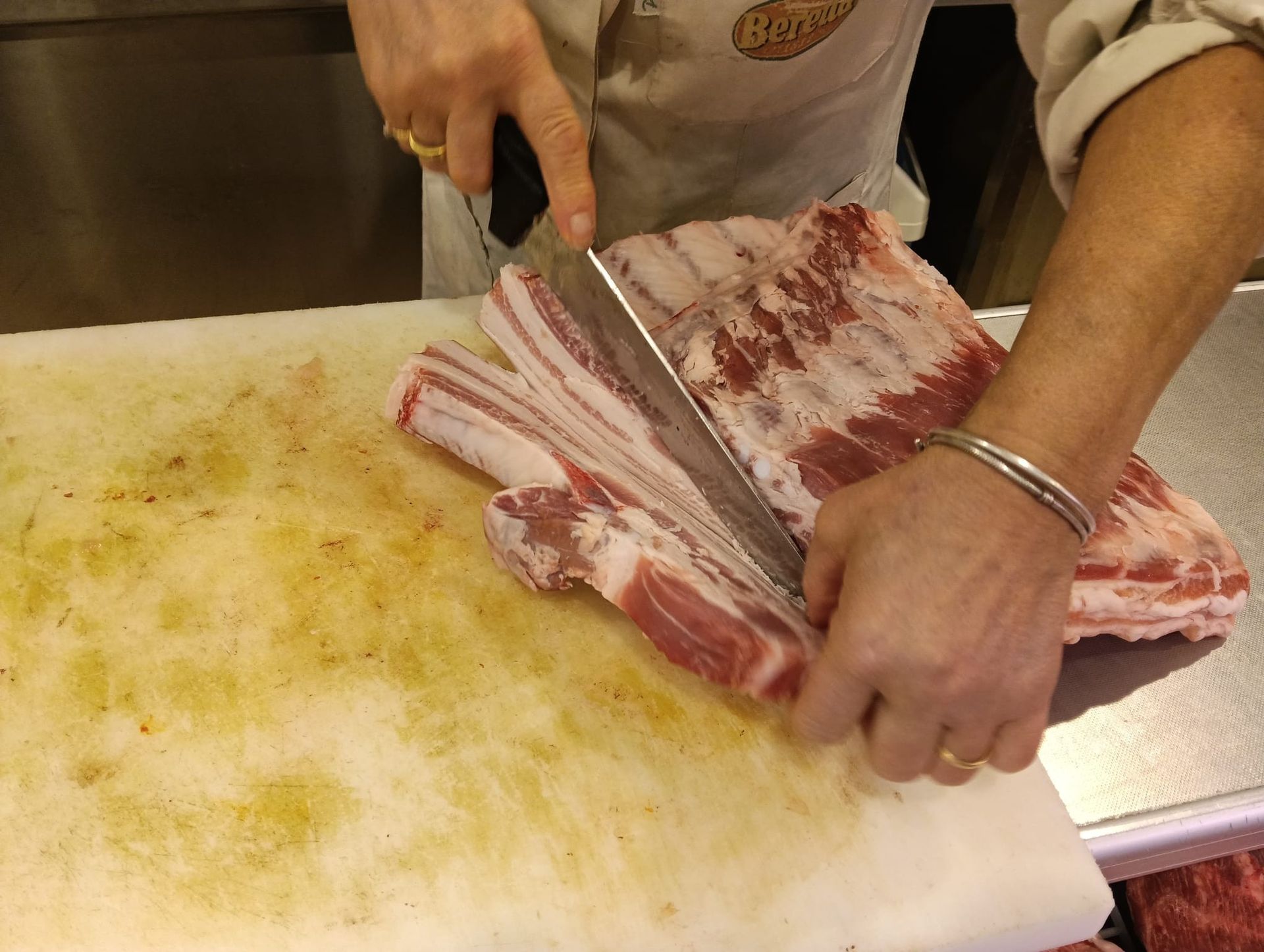 Una persona taglia carne cruda con un grosso coltello su un tagliere bianco.